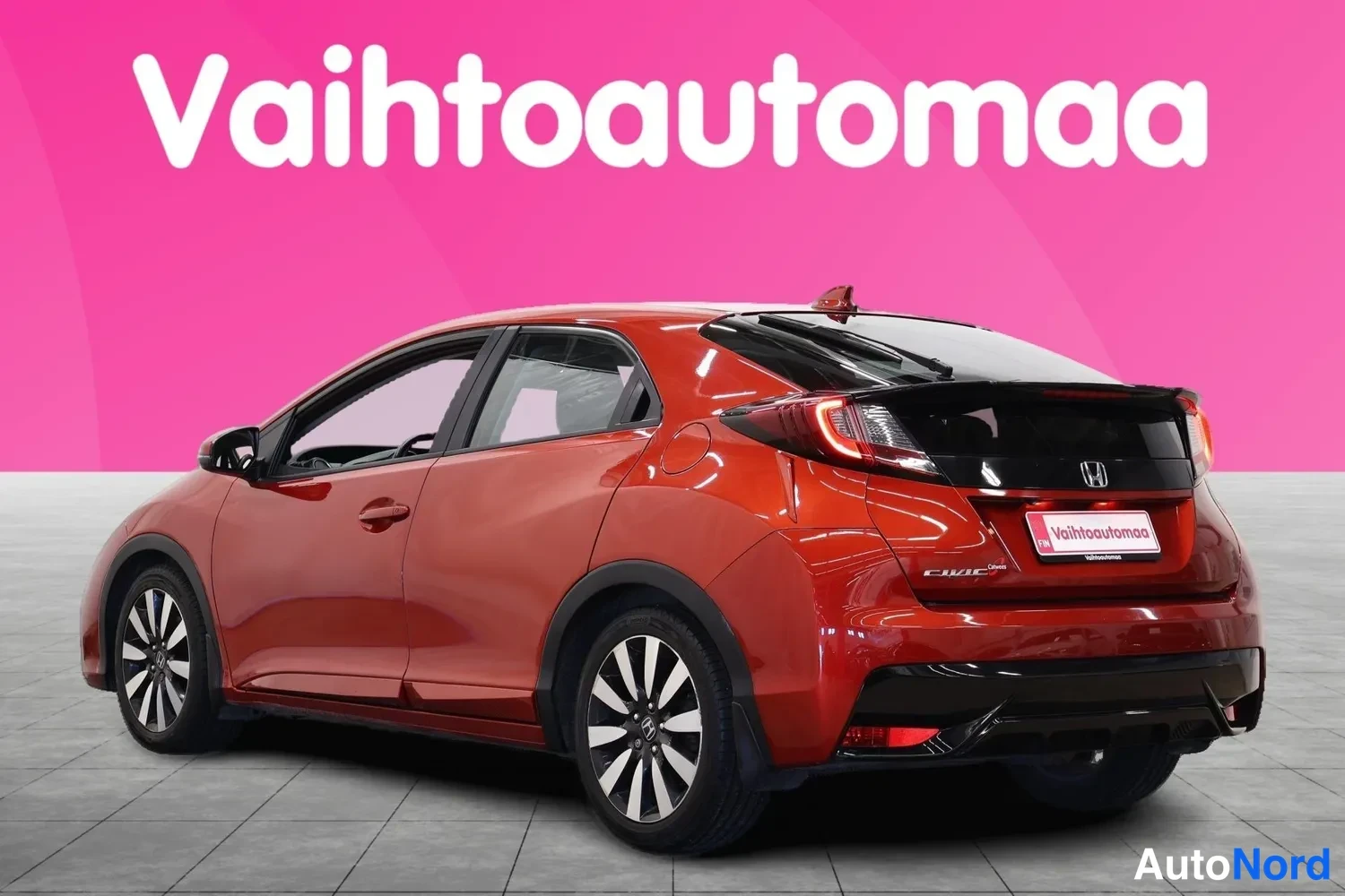 Takaviisto: Punaisen metallicvärinen Honda Civic viistosti takaa vasemmalta kuvattuna, takavalojen ja viistoperän näkyessä.