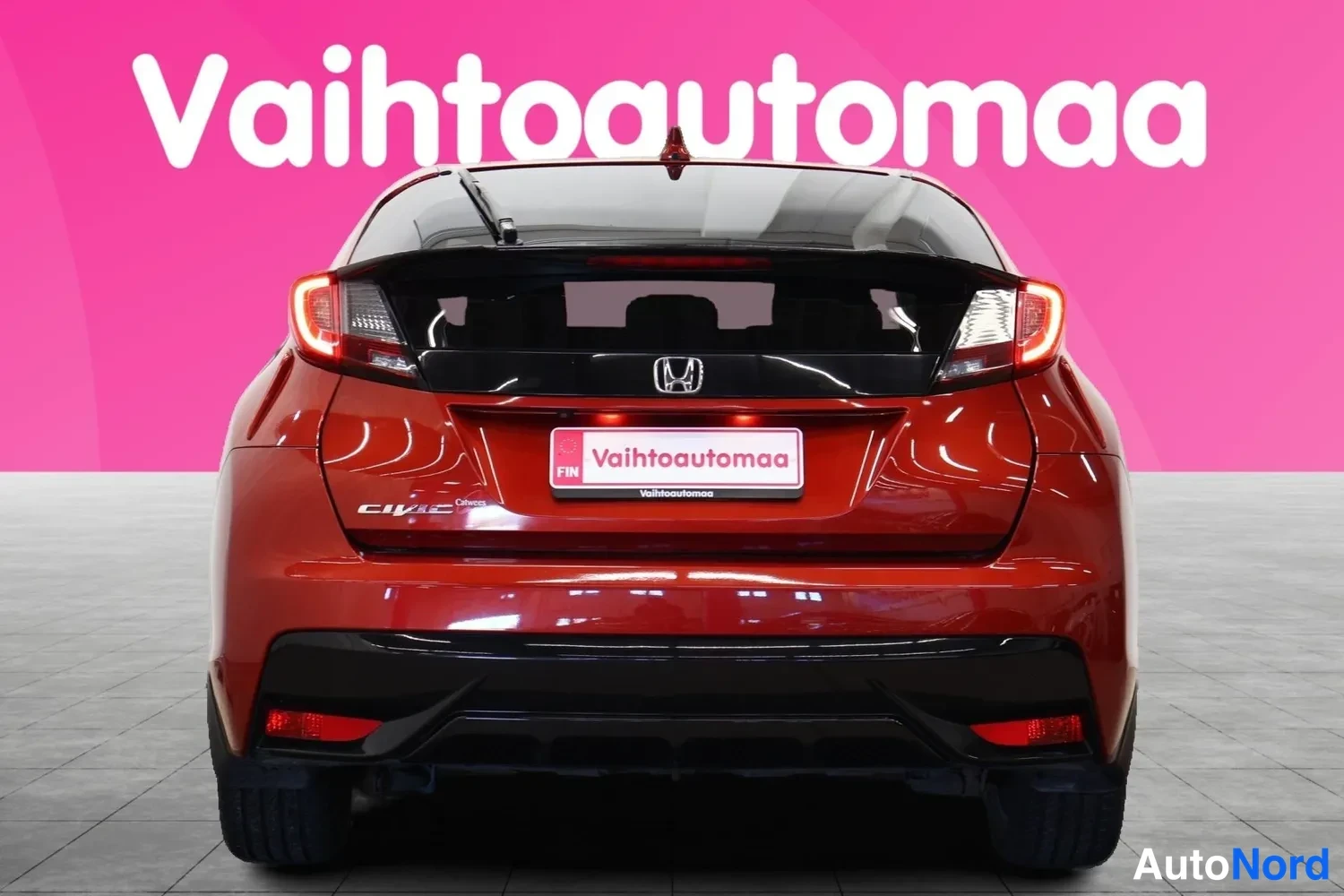 Takaa: Punaisen metallicvärisen Honda Civican takaosa suoraan takaa, takavalojen ja Honda-merkin näkyessä.