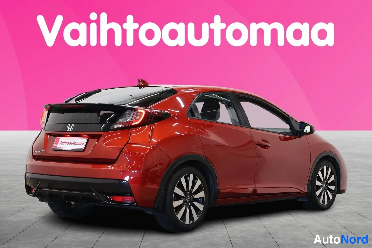 Takaviisto: Punaisen metallicvärinen Honda Civic viistosti takaa oikealta kuvattuna, takavalojen ja kylkien näkyessä.