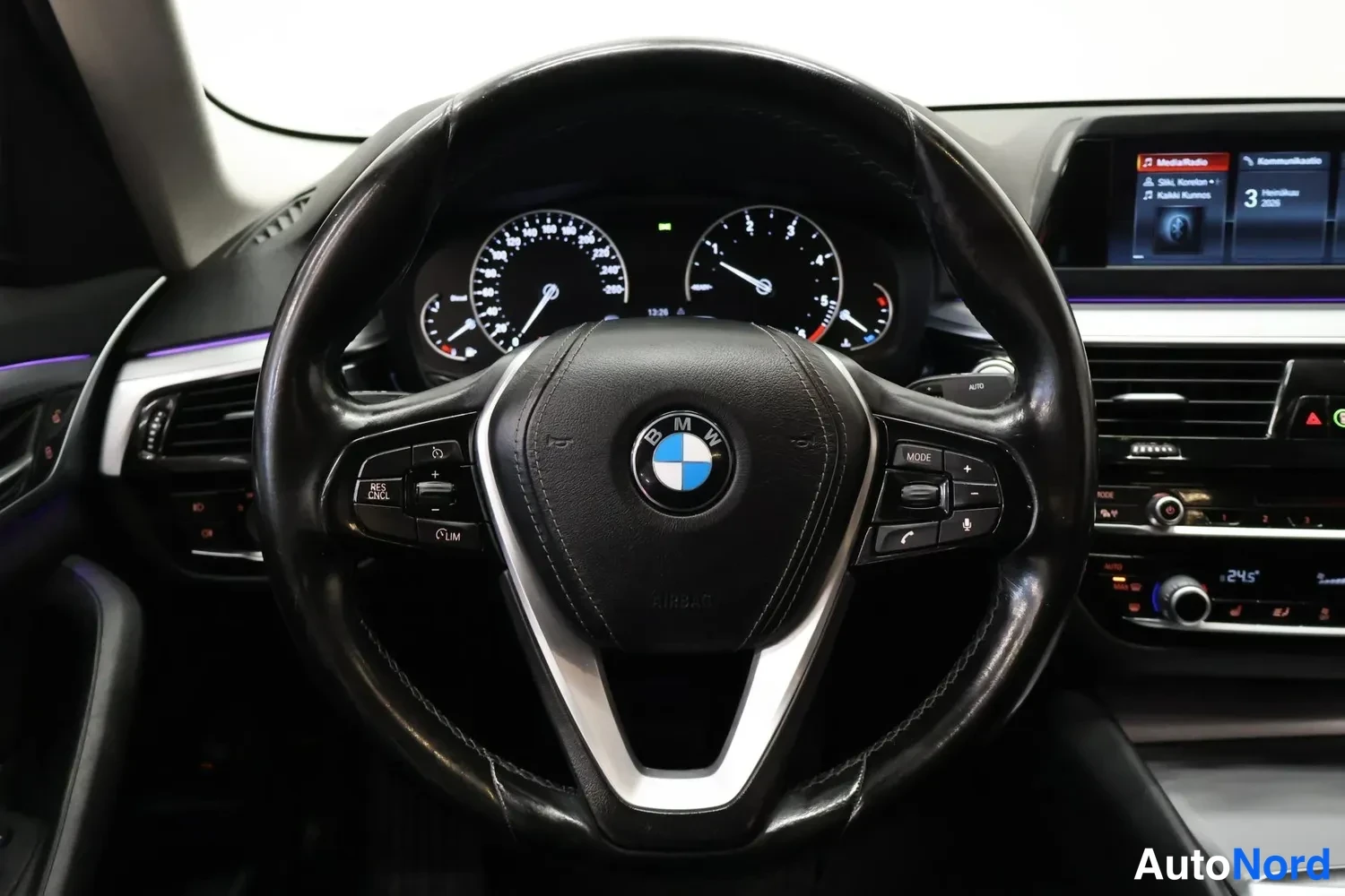 Muu: Ohjauspyörän tarkempi kuva: BMW-merkki keskellä, mittaristo ja infotainment-näyttö taustalla.
