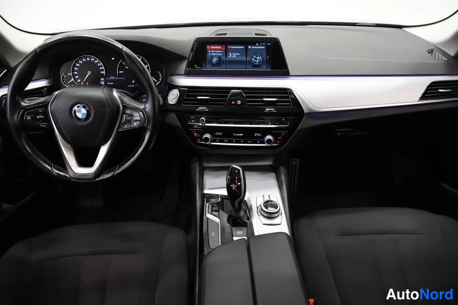 Muu: Ohjaamo ylhäältä: BMW-ohjauspyörä, mittaristo, keskellä kurottava näyttö, ilmastointipaneeli ja vaihtevipu keskikonsolissa.