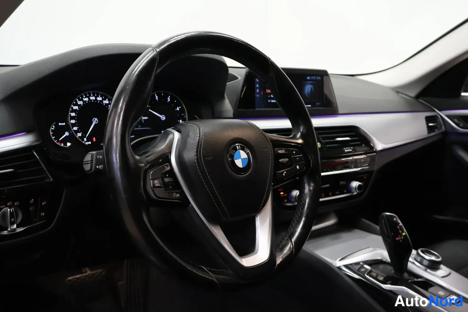 Muu: Ohjaamo nähtynä ohjauspyörän puolelta: BMW-merkki ohjauspyörässä, analogiset mittarit, keskikonsolin näyttö ja vaihtevipu.