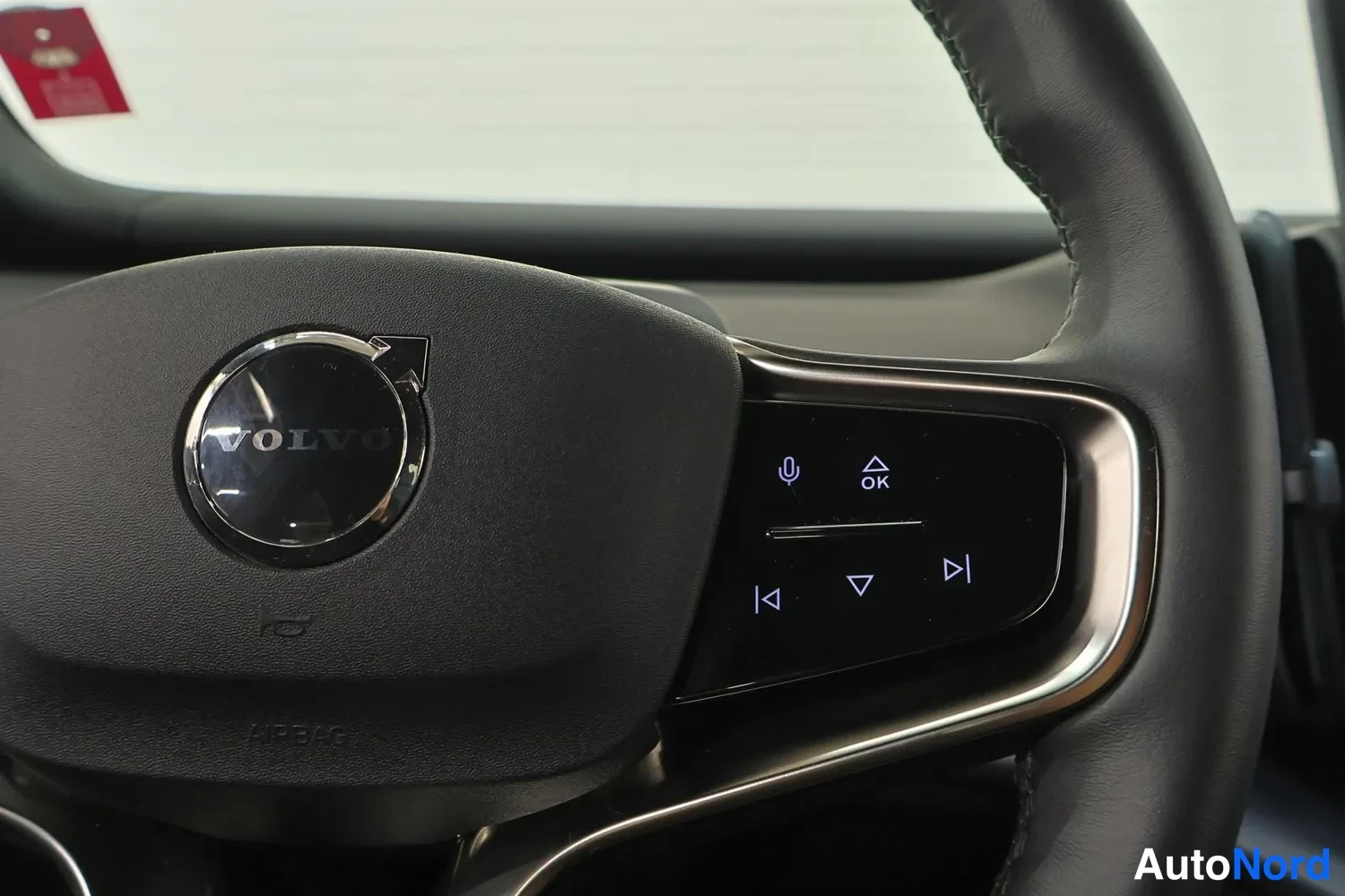 Yksityiskohta: Volvo-merkin ohjauspyörän oikean puolen painikkeet lähikuvassa, taustalla tuulilasi.
