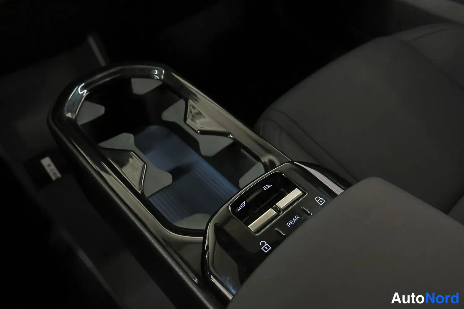 Tavaratila: Top-down view of the gloss black centre console featuring two cupholders with a geometric star pattern and switches for the electric rear tailgate on the armres