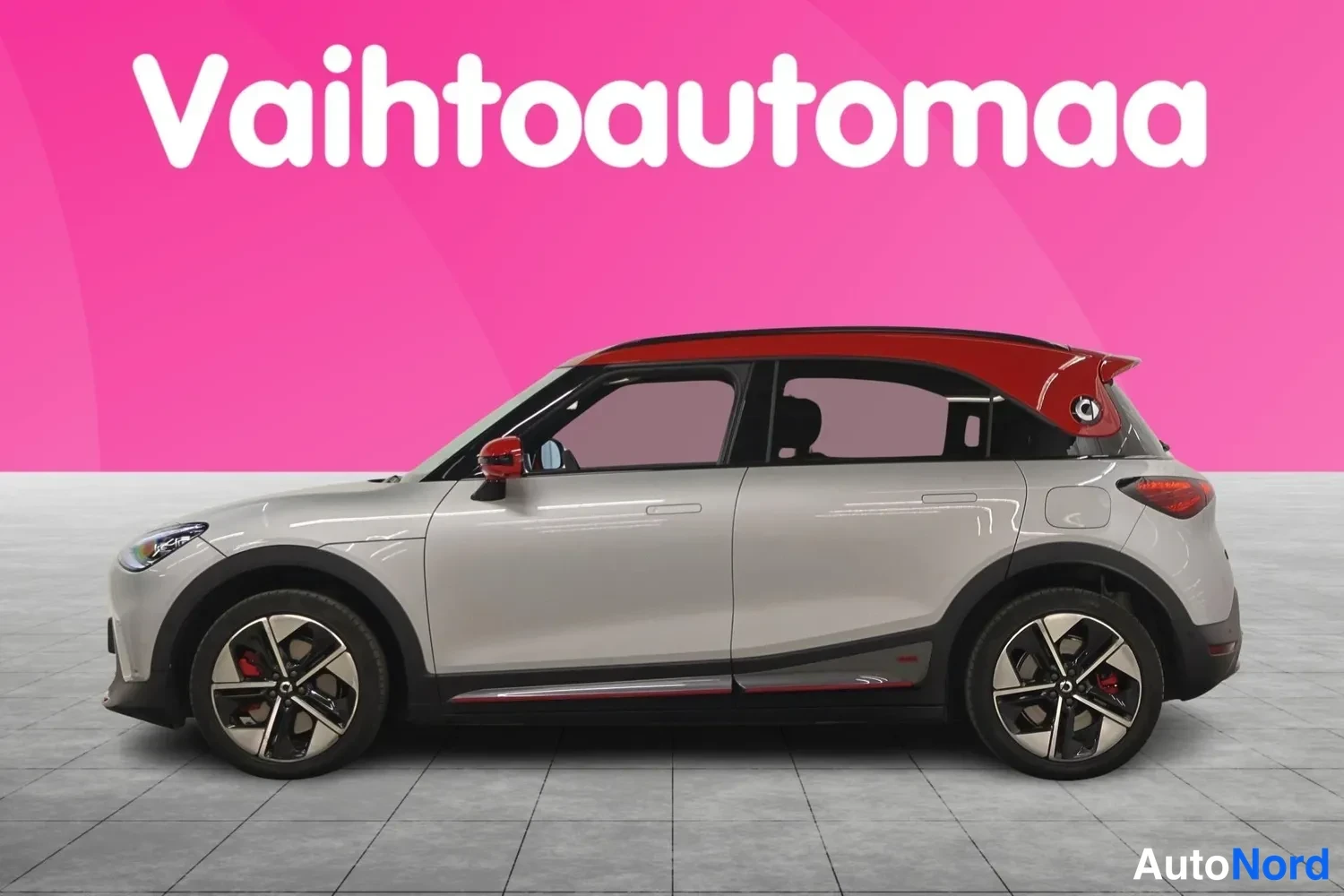 Takaviisto: Smart hillinharmaa crossover sivusta vasemmalta, punainen katto, mustat pölykset, Vahtoautomaan taustalla.