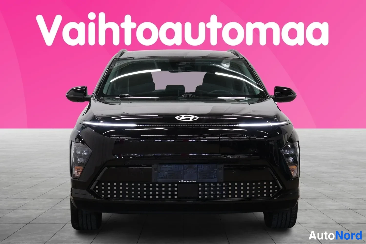 Edestä: Mustan Hyundai Kona -sähköauton suora etunäkymä, LED-vetotulet ja H-merkki konepellissä.