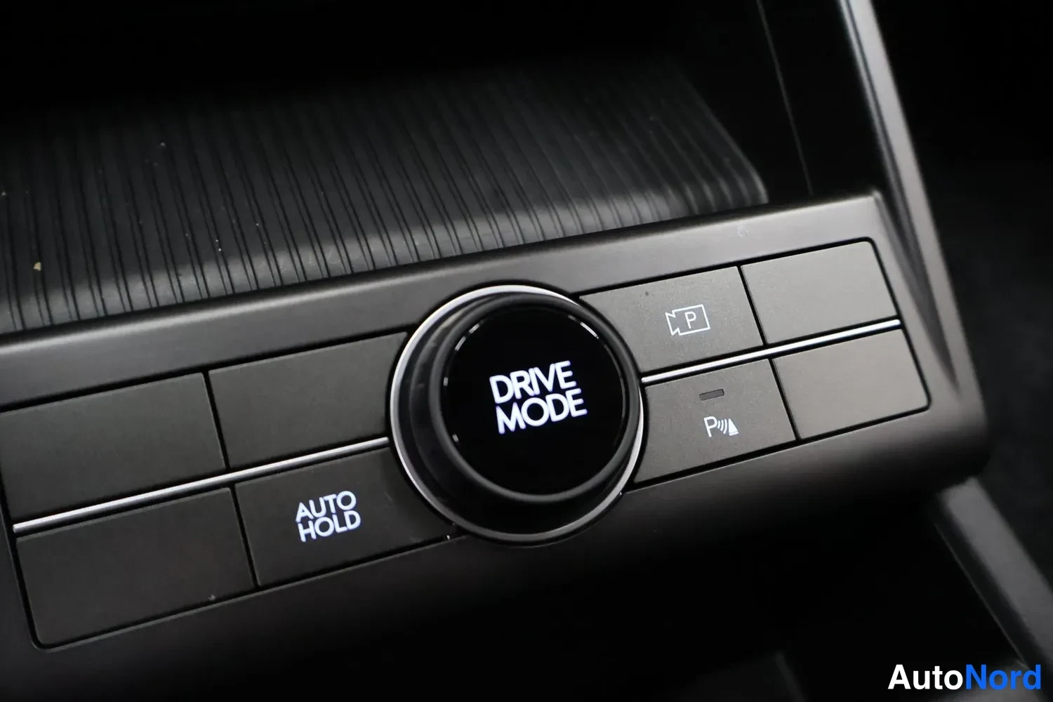 Yksityiskohta: Ohjauspaneeli, jossa on pyöreä 'DRIVE MODE' valitsin, 'AUTO HOLD' painike ja 'P' symbolilla varustettu painike.