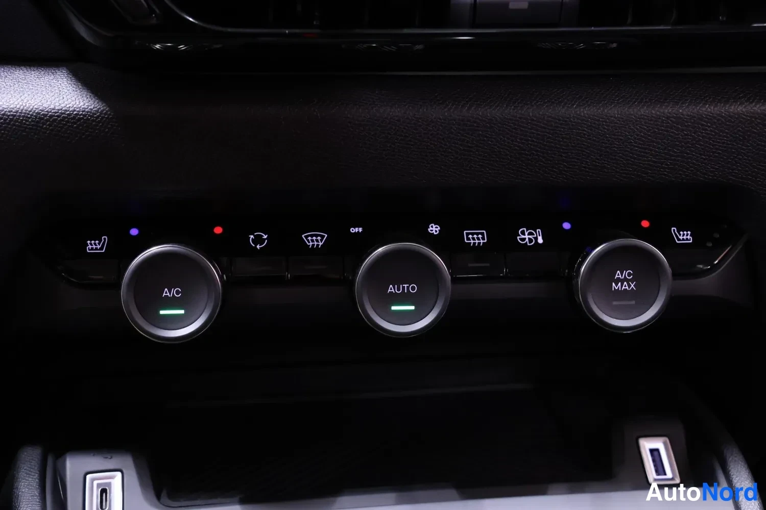 Muu: Keskikonsolin ilmastointipainikkeet lähikuvassa: A/C-, AUTO- ja A/C MAX-pyorörönapit sekä tuulilasin sulatus- ja istuinlämmitysmerkit.