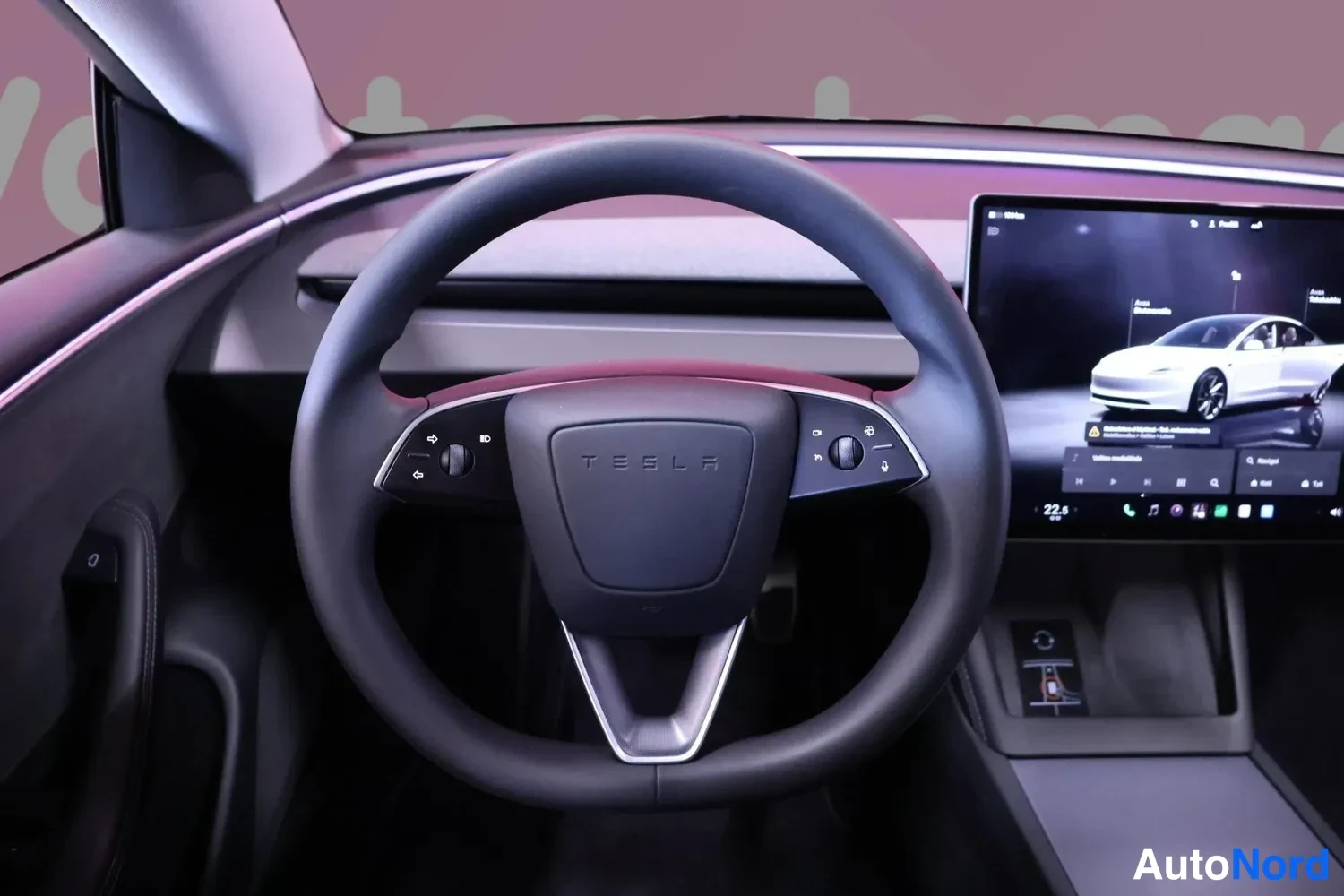 Muu: Lähikuva ohjauspyörästä, jossa TESLA-logo ja painikkeet; taustalla kosketusnäyttö, jossa 3D-auton kuva.