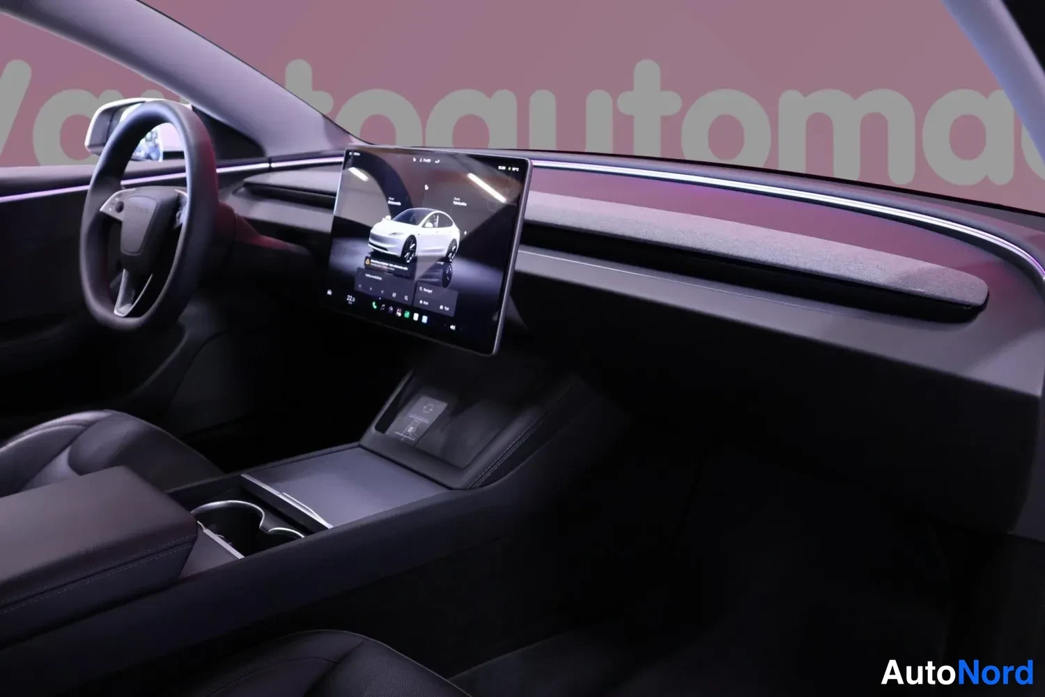 Muu: Tesla Model 3:n sisätilat: tumma dashboardi, ohjauspyörä vasemmalla ja keskiruutu näyttää auton mallia.