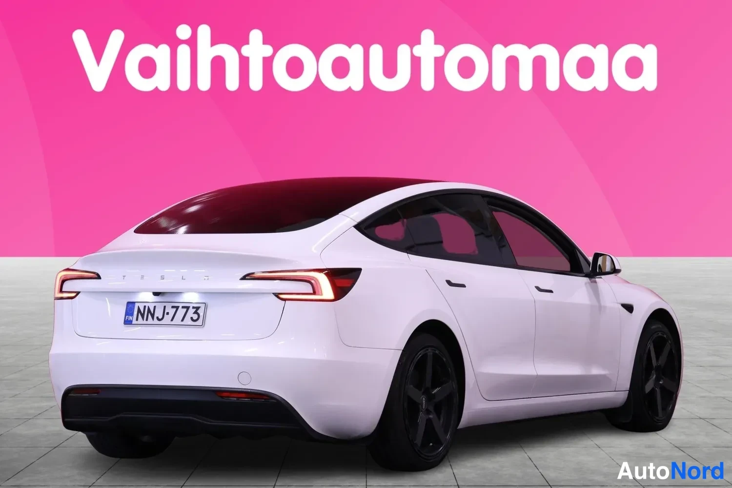 Takaviisto: Valkoinen Tesla Model 3 -henkilöauto takaa vasemmalta vinosti, rekisterilla.