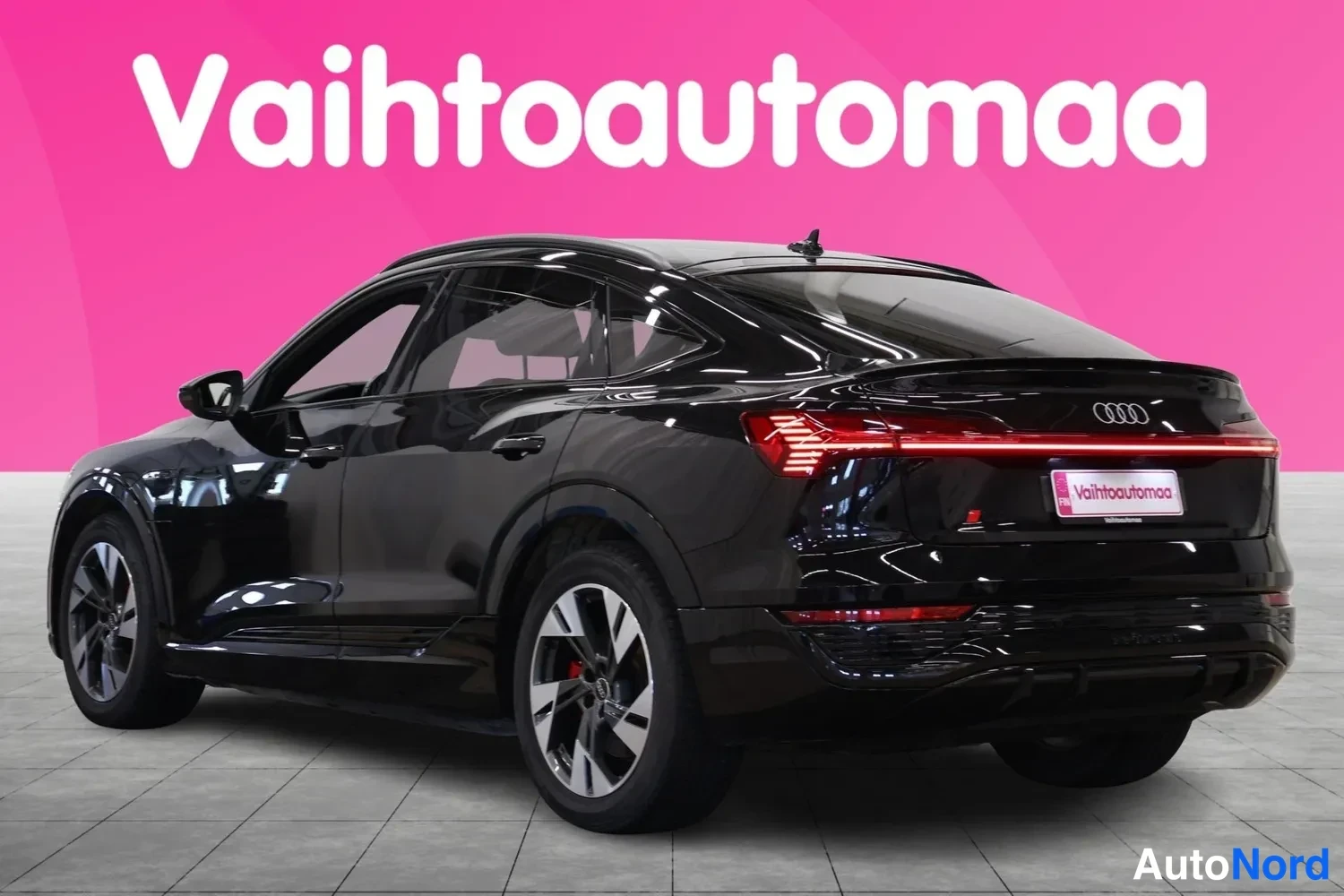 Takaviisto: Mustan Audin takakulmakuva vasemmalta, poikittainen punainen takavalotanko ja Audi-merkki, Vaihtoautomaan kilpi takaluukussa.