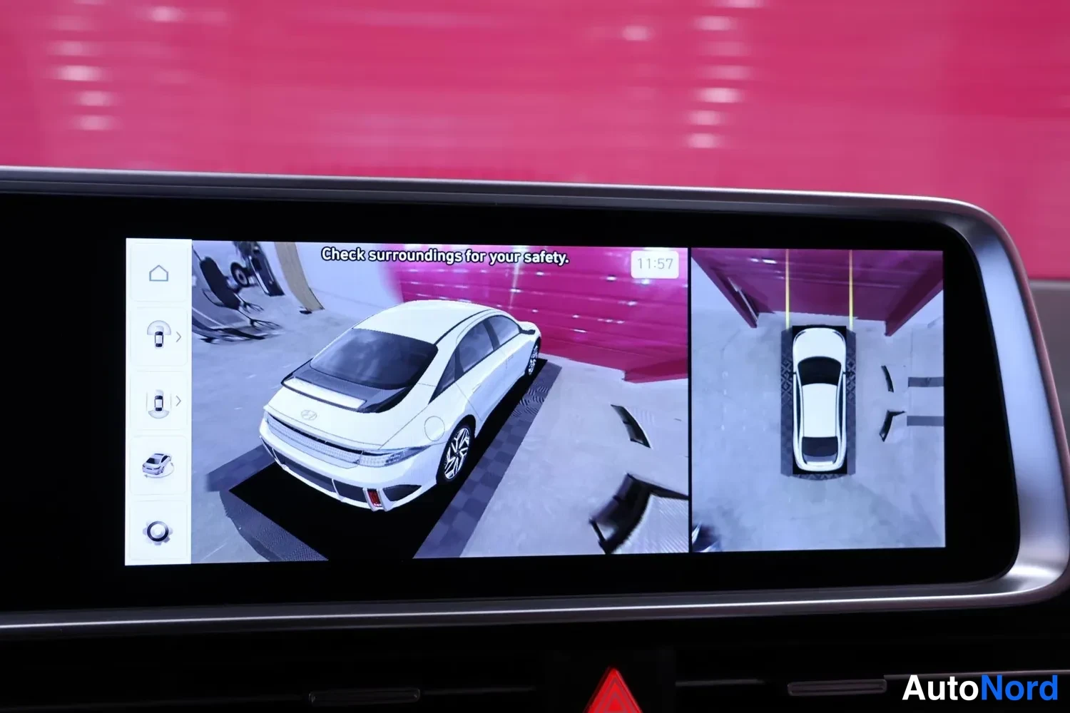 Ohjaamo: Dashboard display showing a split-screen 360-degree camera view of the white vehicle with text 'Check surroundings for your safety' and time '11:57'