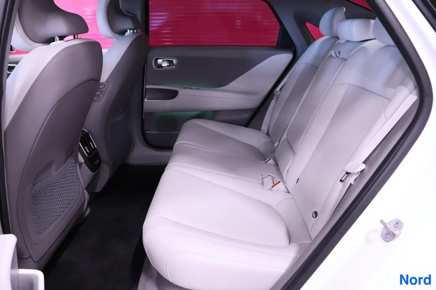 Takaistuimet: Rear passenger cabin showing white bench seat spanning the width with two headrests and integrated seatbelts; grey front seat backs visible in foreground