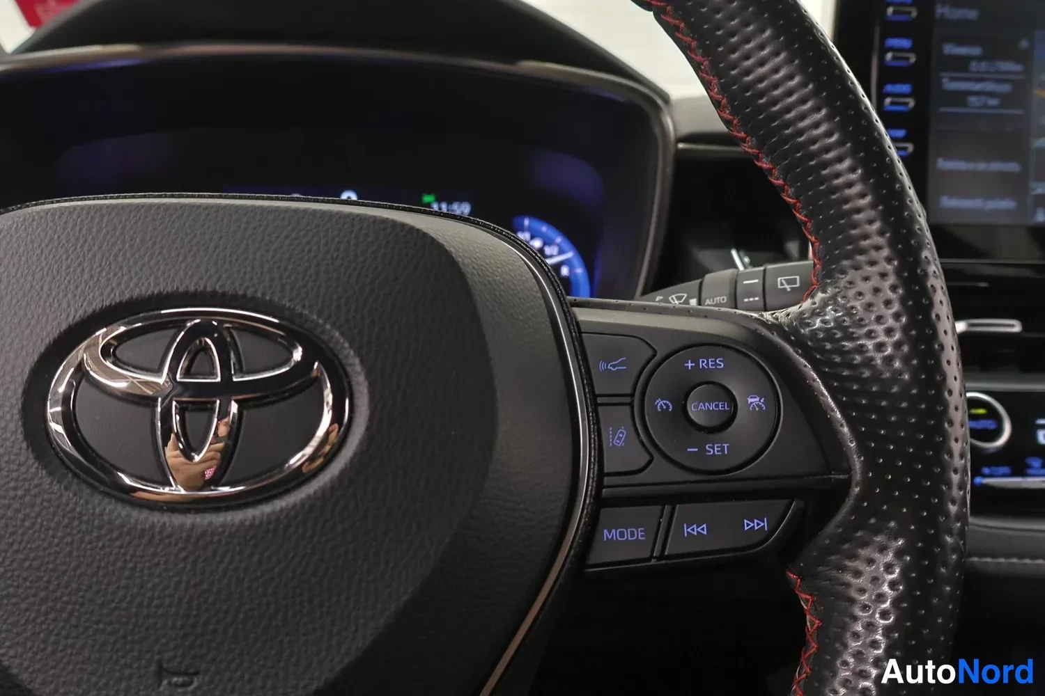Muu: Toyota-merkkiohjauspyörän keskusta ja oikean pujottelunappi, jossa vakionopeudensäädin RES/CANCEL/SET ja MODE- ja äänitunnisteet; taustalla osittain näkyvä mitt