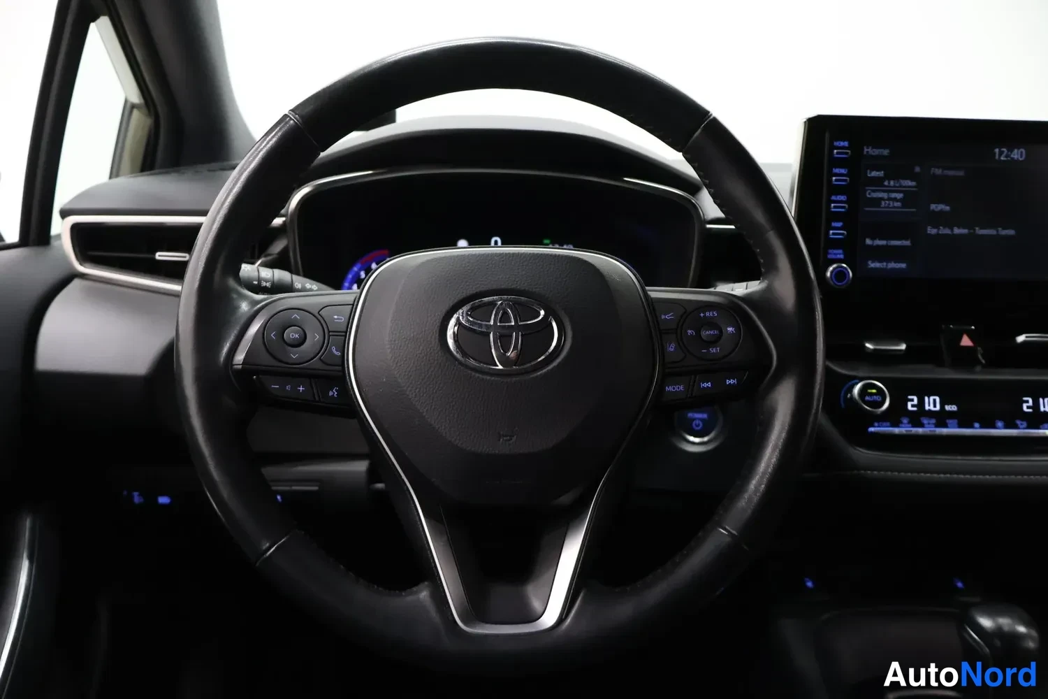 Sivulta: Ohjauspyörän lähikuva Toyota-merkillä, napit ja käynnistyspainike näkyvät.