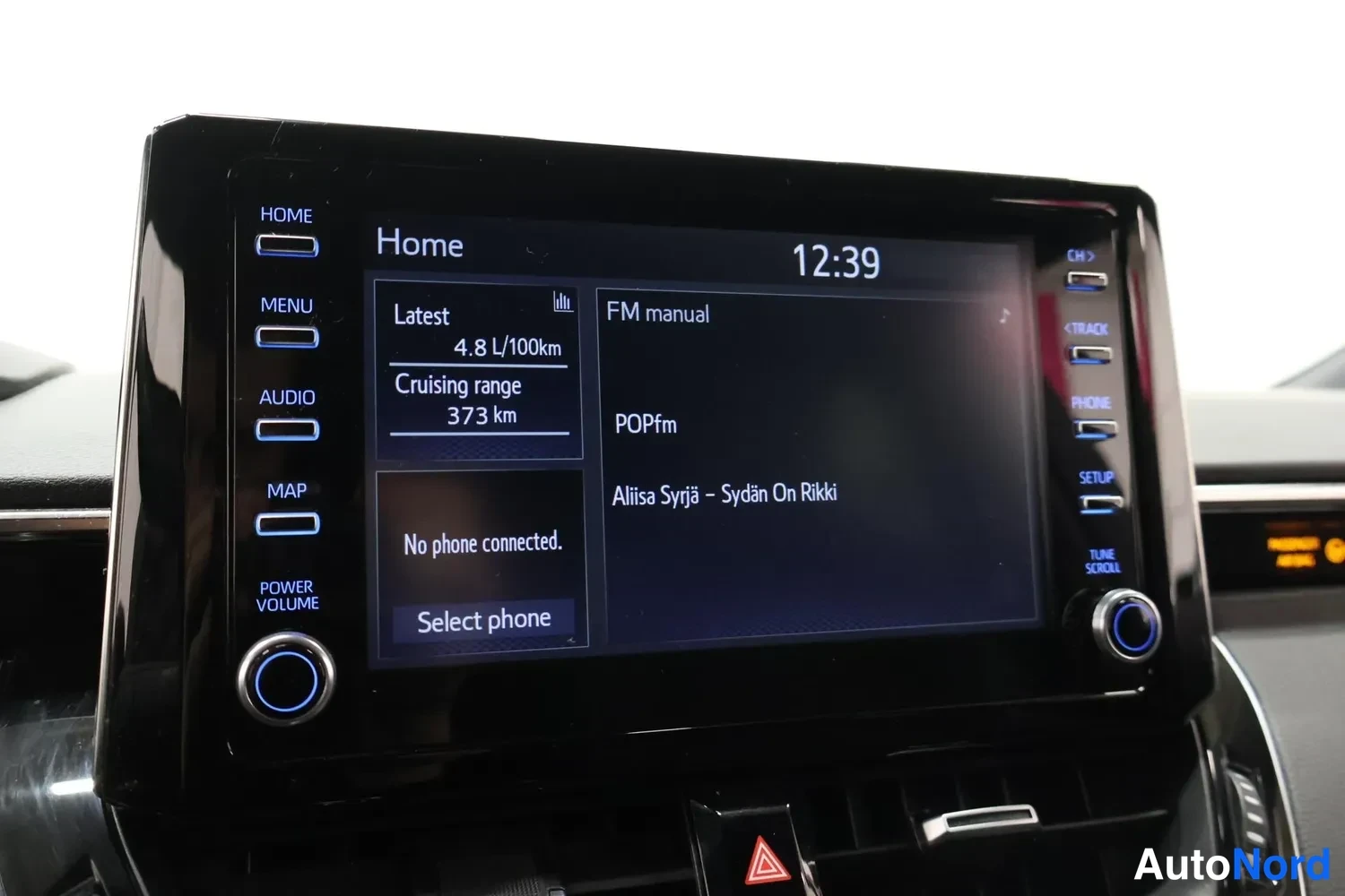 Yksityiskohta: Infotainment-näyttö näyttää kotinäkymän: keskiarvo 4,8 L/100 km, ajo 373 km, FM-radio ja APE-artisti.