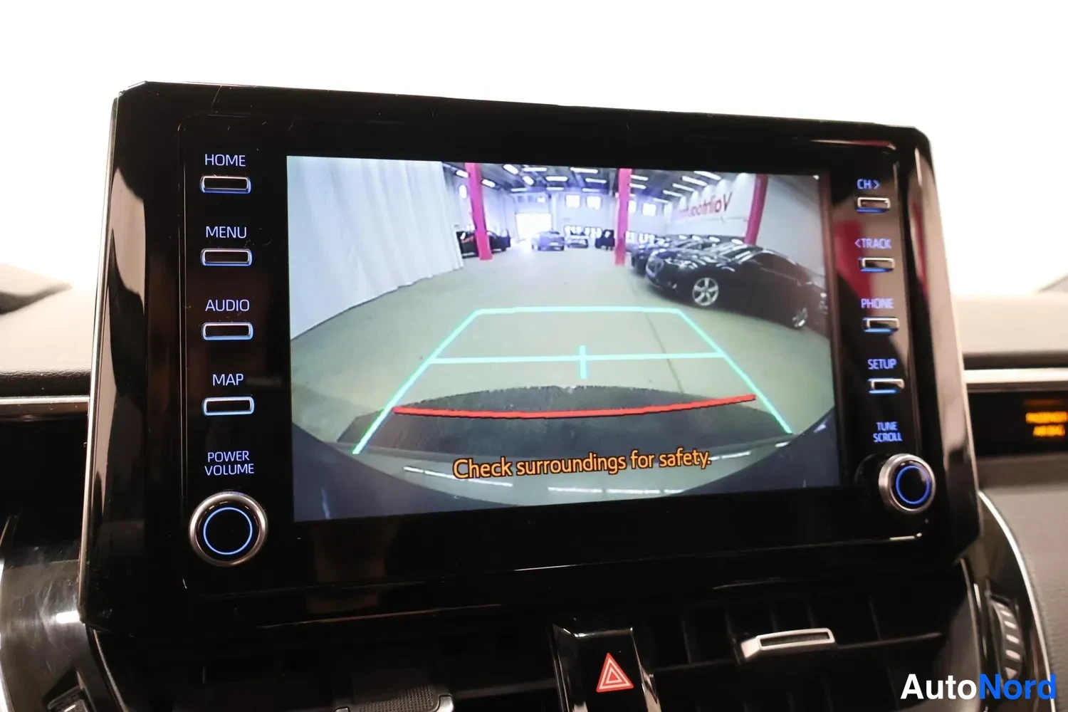 Yksityiskohta: Infotainment-näyttö näyttää peruutuskameran kuvan apuviivoineen ja tekstin 'Check surroundings for safety'.