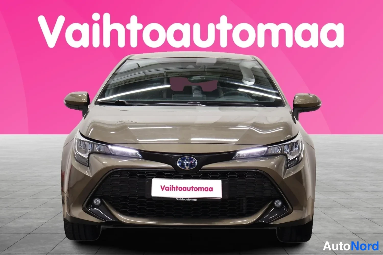 Edestä: Ruskean-beige Toyota Corolla suoraan edestä, Toyota-merkki ja logollinen rekisterikilpi