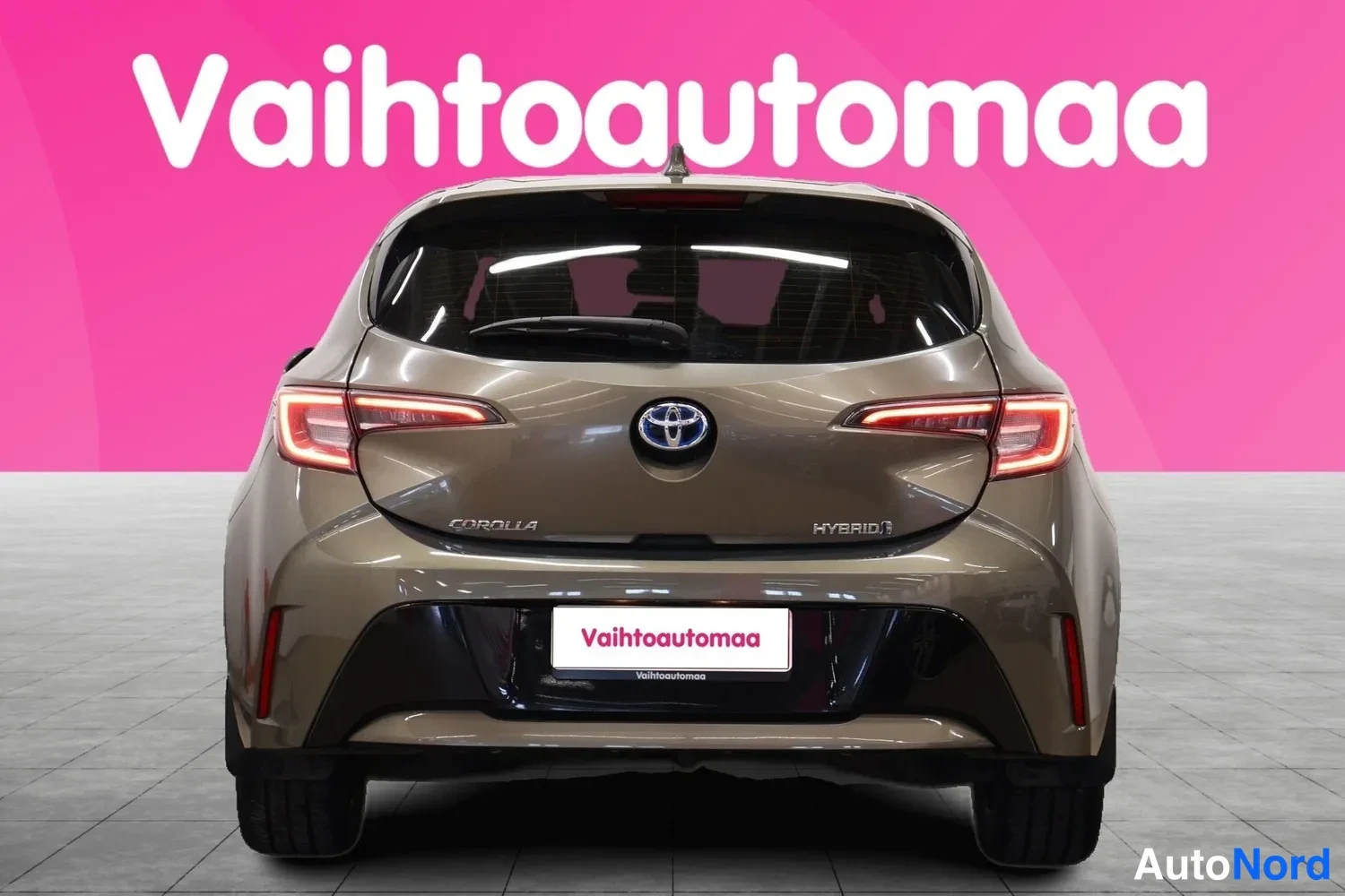 Takaa: Auto suoraan takaa kuvattuna: ruskea koripinta, takavalot, Toyotan merkki, COROLLA- ja HYBRID-tekstit.