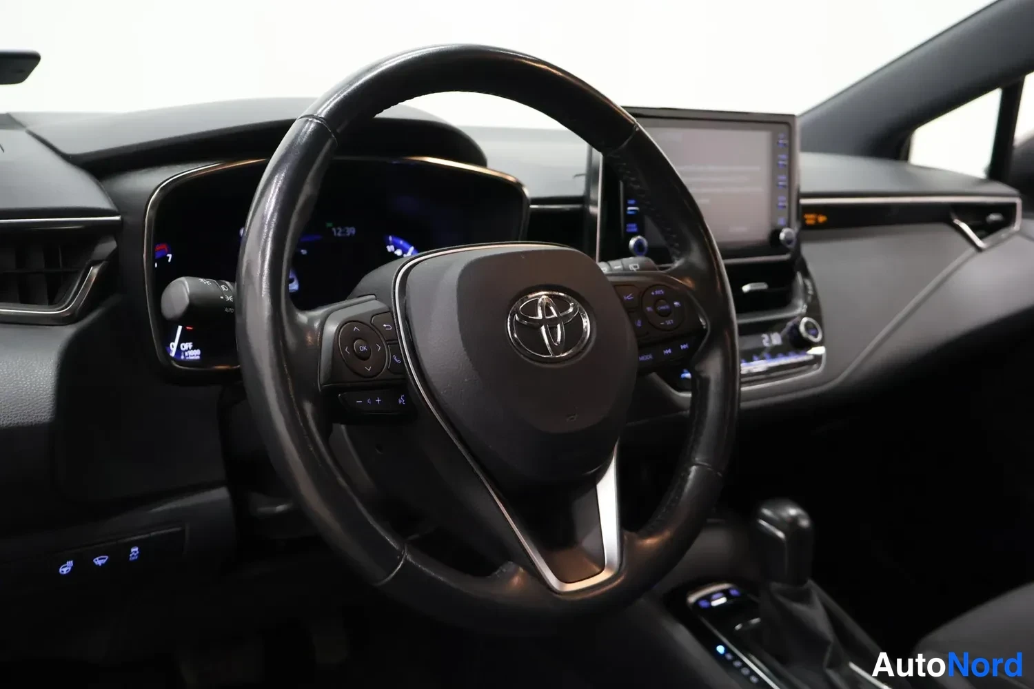 Sivulta: Kuljettajan näkymä: Toyota-merkkinen ohjauspyörä, mittaristo ja kosketusnäyttö keskikonsolissa.