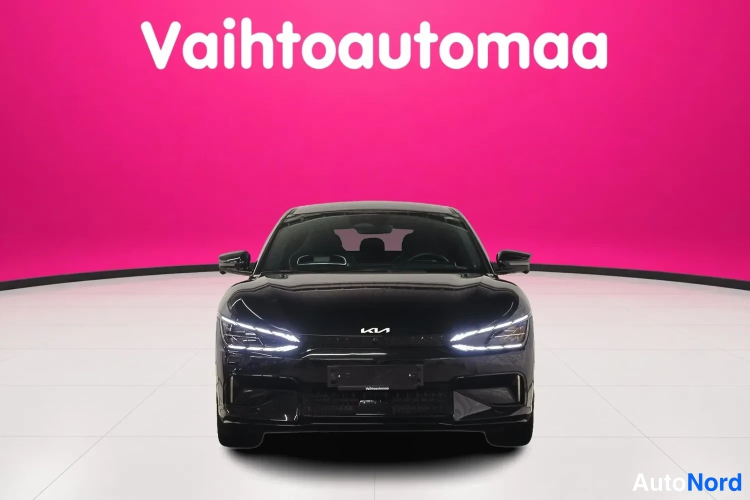 Edestä: Mustan Kia EV6:n etunäkymä suoraan edestä päin, Vahtoautomaan taustalla.