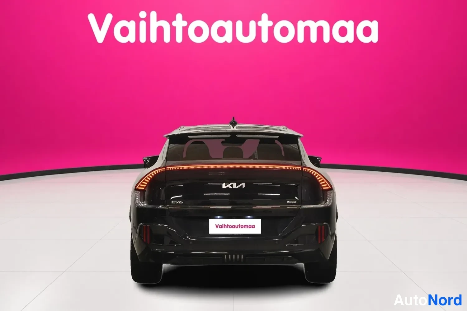 Takaa: Mustan Kia EV6:n takaosa suoraan takaa, vaalikkuvat takavalot ja KIA-merkki näkyvät pinkkib taustaa vasten.