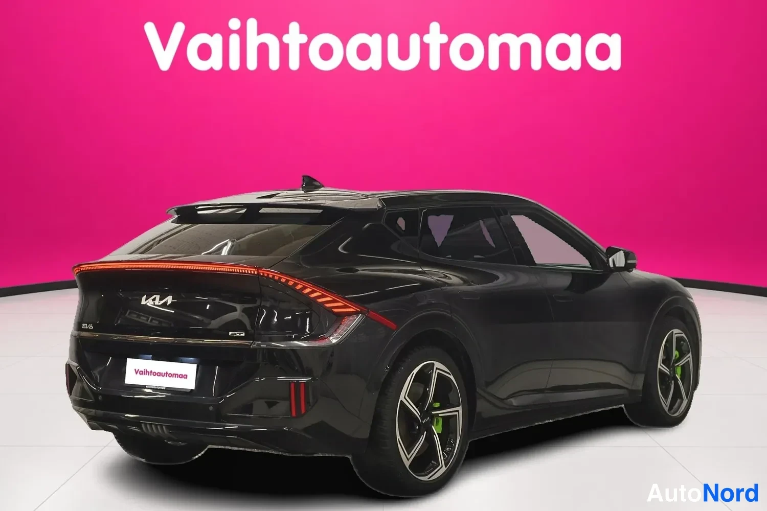 Takaviisto: Mustan henkilöauton takaosa ja kylki kolmanneskulmasta: pitkä takavalojauova, Kia-merkki perällä ja tummat kevytmetallivanteet, tausta pinkki.