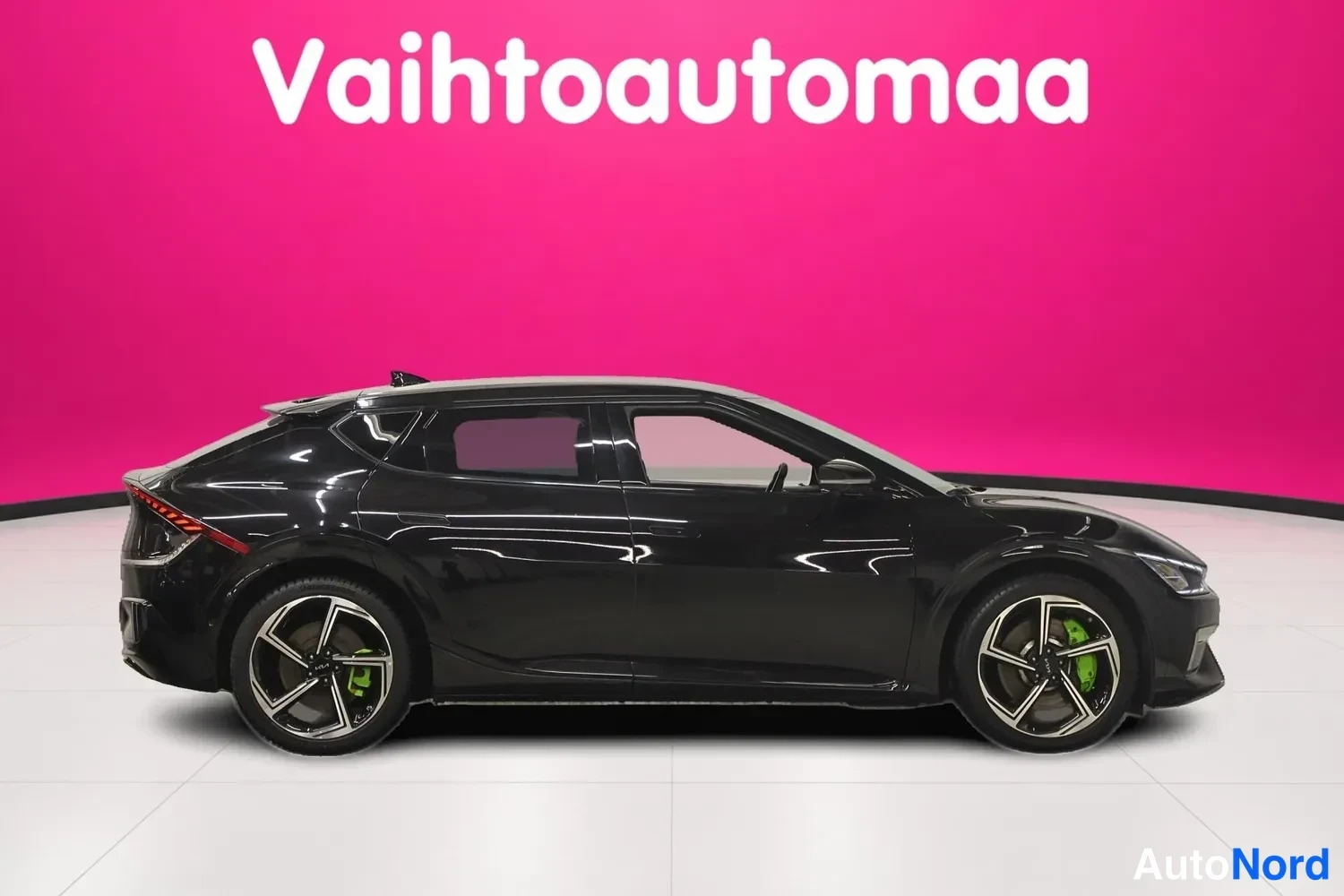 Sivulta: Mustan henkilöauton kylki suoraan sivulta; tummat kevytmetallivanteet ja vihreät jarrusatulat erottuvat, tausta pinkki.