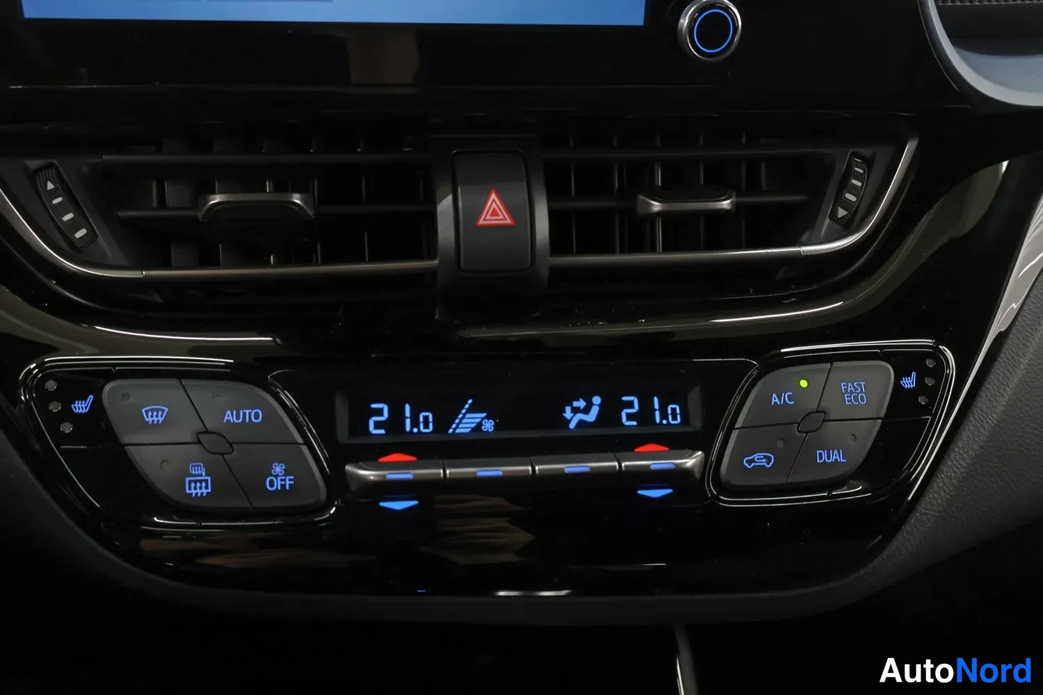 Muu: Auton kojelaudan ilmastointipaneeli näytöllä lukemat 21,0 ja 21,0; napit A/C, DUAL, AUTO ja OFF, osa napeista valaistu sinisellä.
