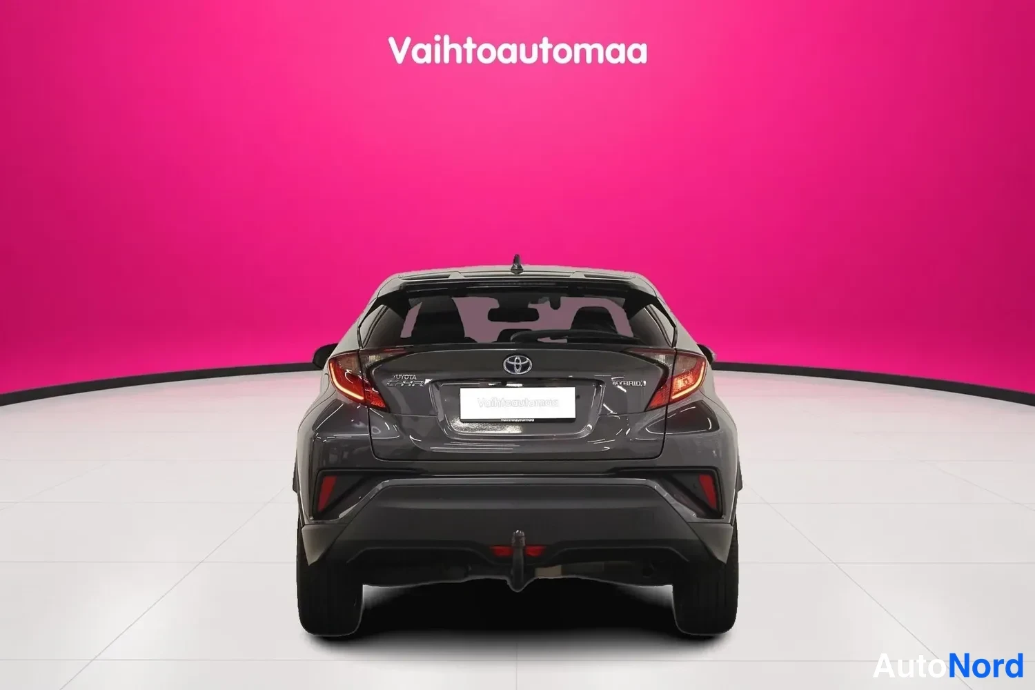 Takaa: Tummanharmaa Toyota C-HR suoraan takaa, peräosa ja takavalot näkyvissä, tummanpunainen tausta.