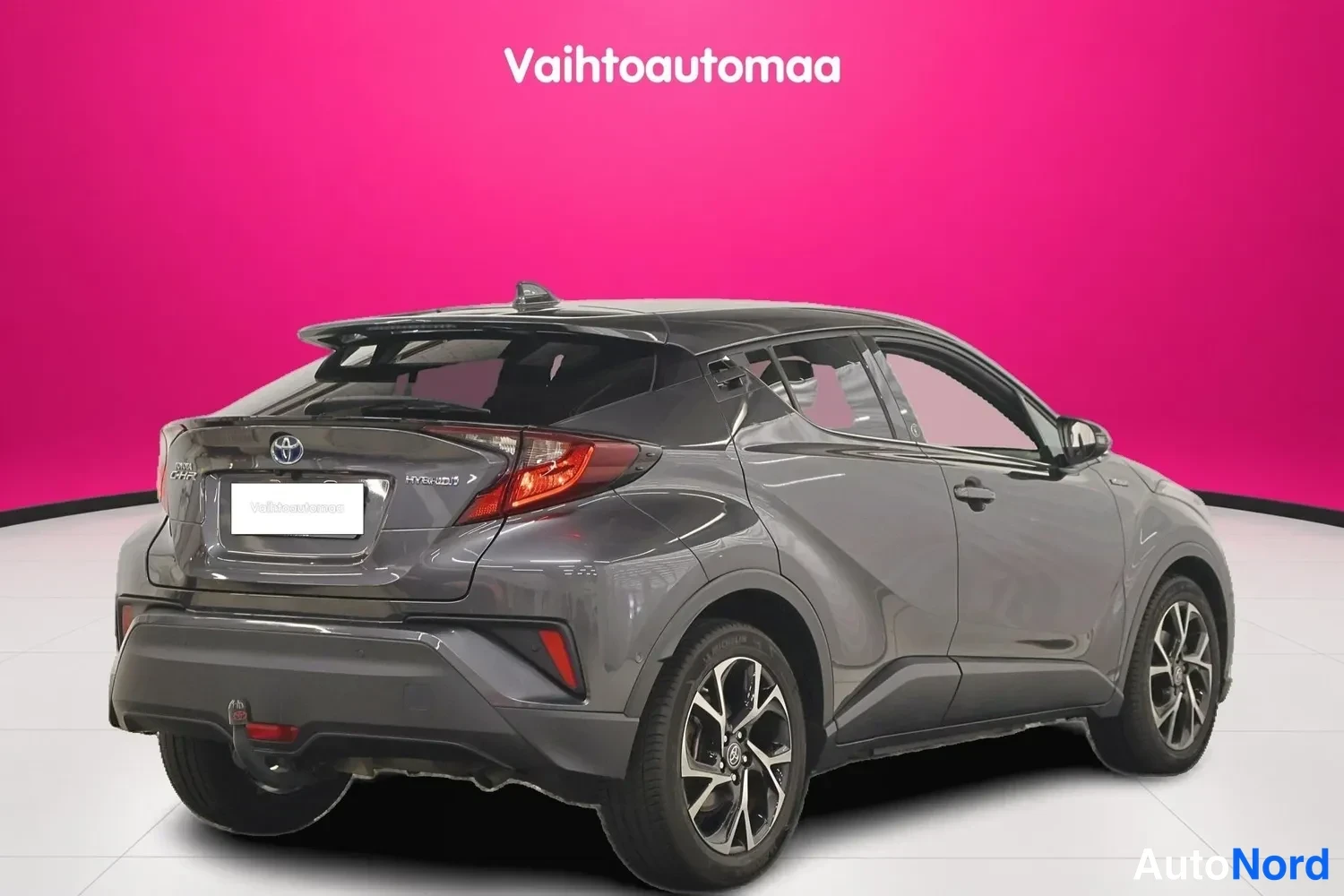 Takaviisto: Auton takaosa ja vasen kylki vinosta takanurkkakulmasta: tummanharmaa Toyota C-HR, hybrid-merkintä takaluukussa, hytkypukki takapuskurissa.