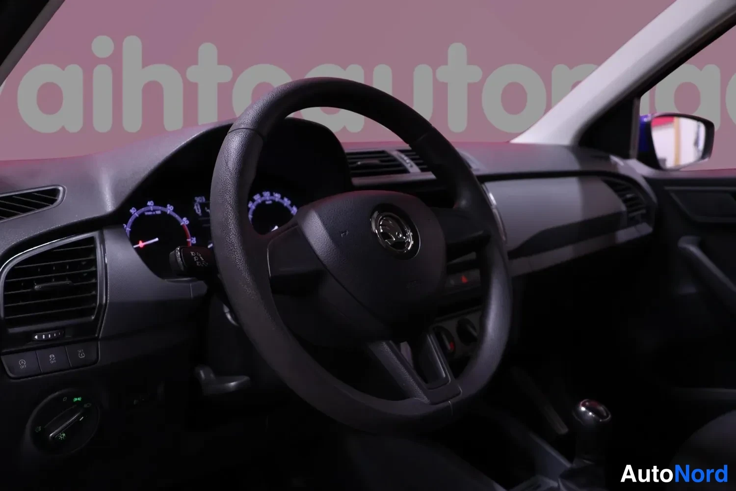 Muu: Ohjaamo sivulta: Skoda-ohjauspyörä, mittarit valaistuna, radio ja manuaalivaihteiston vaihdekeppi.