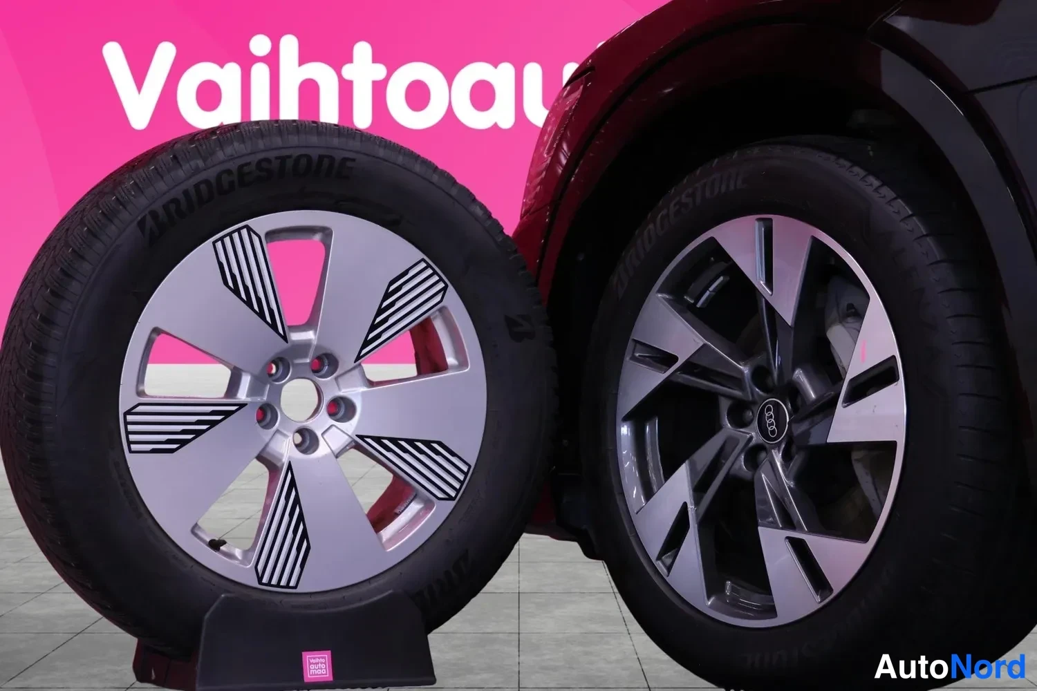 Yksityiskohta: Sivuilta irrotettu Bridgestone-renkaalla varustettu hopeavannes levyjarruvalitsin nayttetaan ajoneuvon pyoran vieressa pinkilla taustalla.