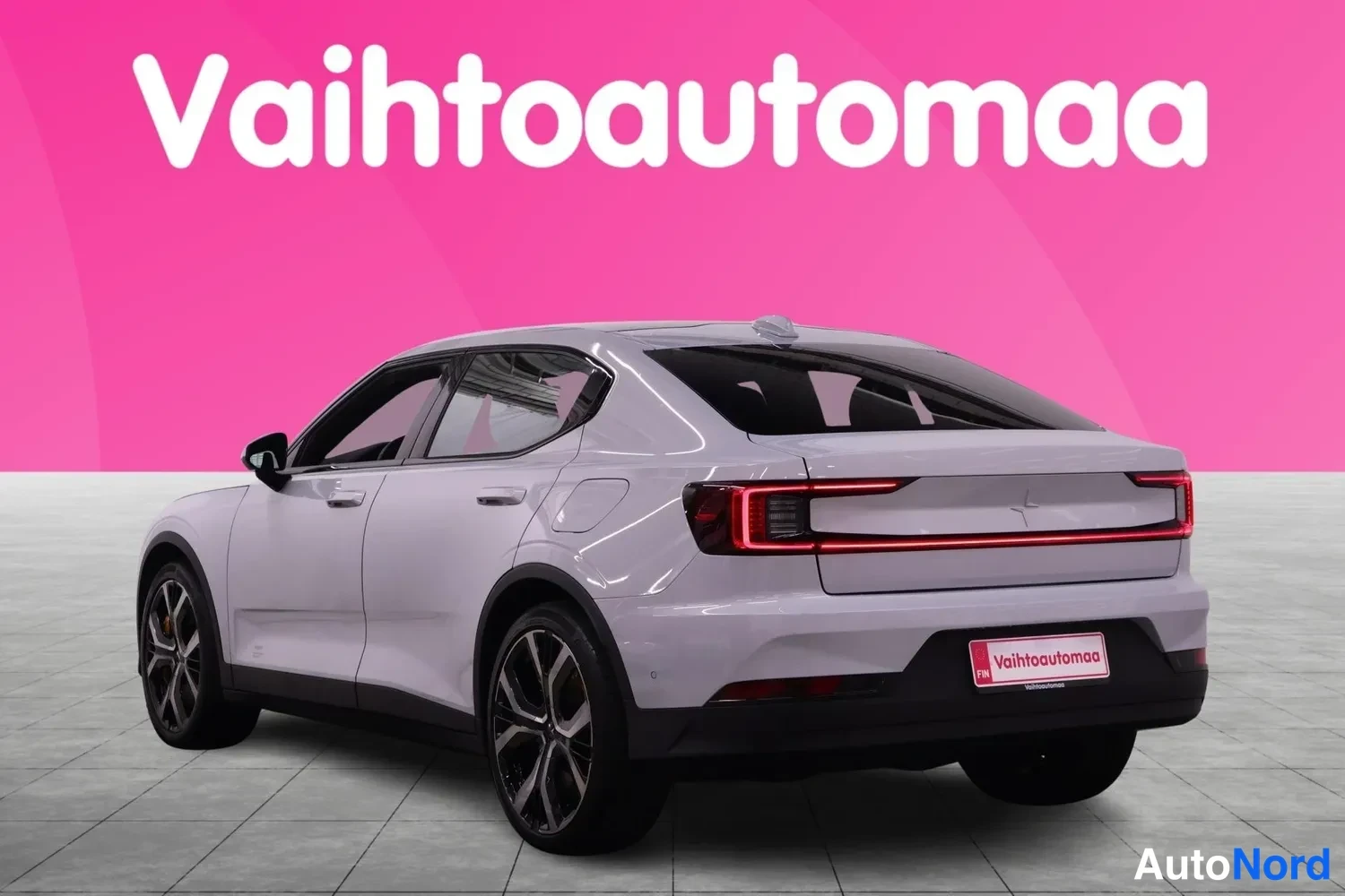 Takaviisto: Auton takaosakolmiväl: vaaleanharmaa korpi, Vahtoautomaa-kyltti takapuskurissa ja tummat kevytmetallivanteet näkyvät studiotyttötaustaa vasten.