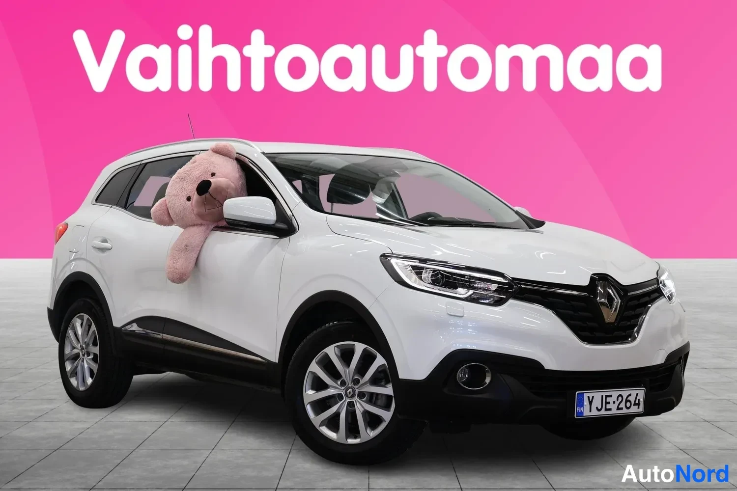 Etuviisto, nokka oikealle: Valkoinen Renault Kadjar etukulmasta oikealta, rekisteritunnuksella, vaaleanpunaisella taustalla.