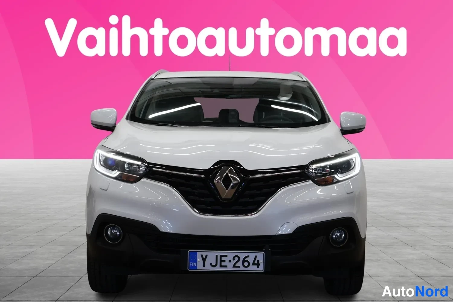 Edestä: Valkoinen Renault Kadjar suoraan edestäpäin, rekisteritunnuksella, vaaleanpunaisella taustalla.