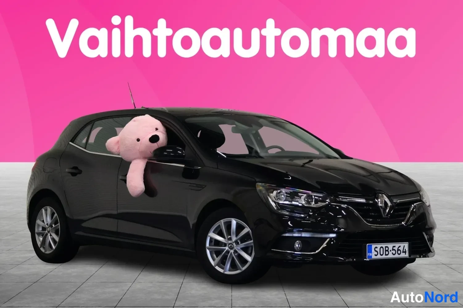 Etuviisto, nokka oikealle: Musta Renault Megane -henkinen viistosti edestä vasemmalta kuvattu henkilöauto pinkillä taustalla, rekisterikilpi S0B-564.