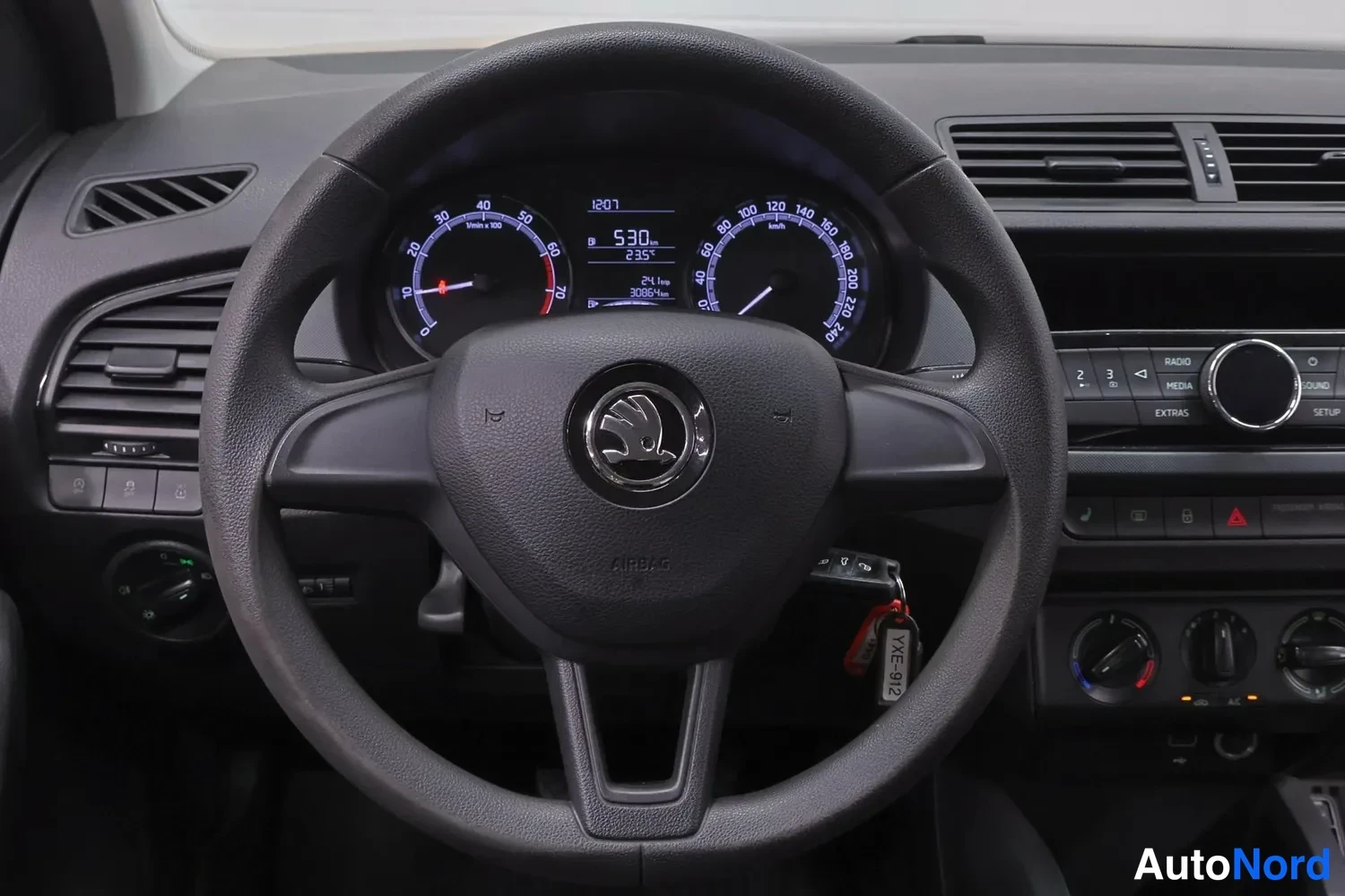 Muu: Ohjaamon lähikuva: Skoda-merkkinen ohjauspyörä, jonka takana mittaristo näyttää lukeman 530, kellonajan 12:01 ja lämpötilan 23,5 °C. Sytytysavain on paikallaan