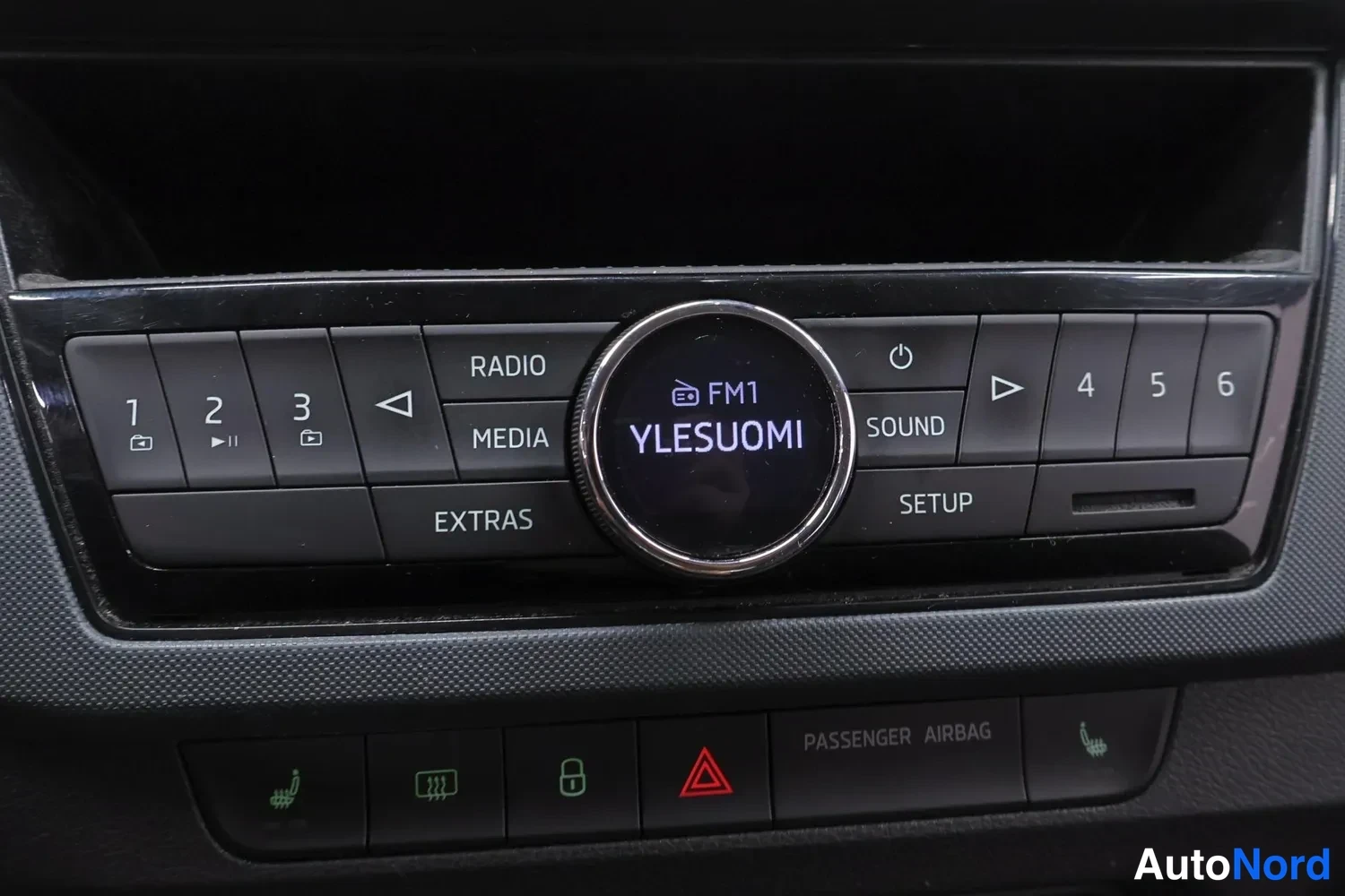 Ohjaamo: Dashboard focus on the car radio unit, showing a central screen that reads YLESUOMI. Buttons for RADIO, MEDIA and EXTRAS are visible below. The hazard warning l