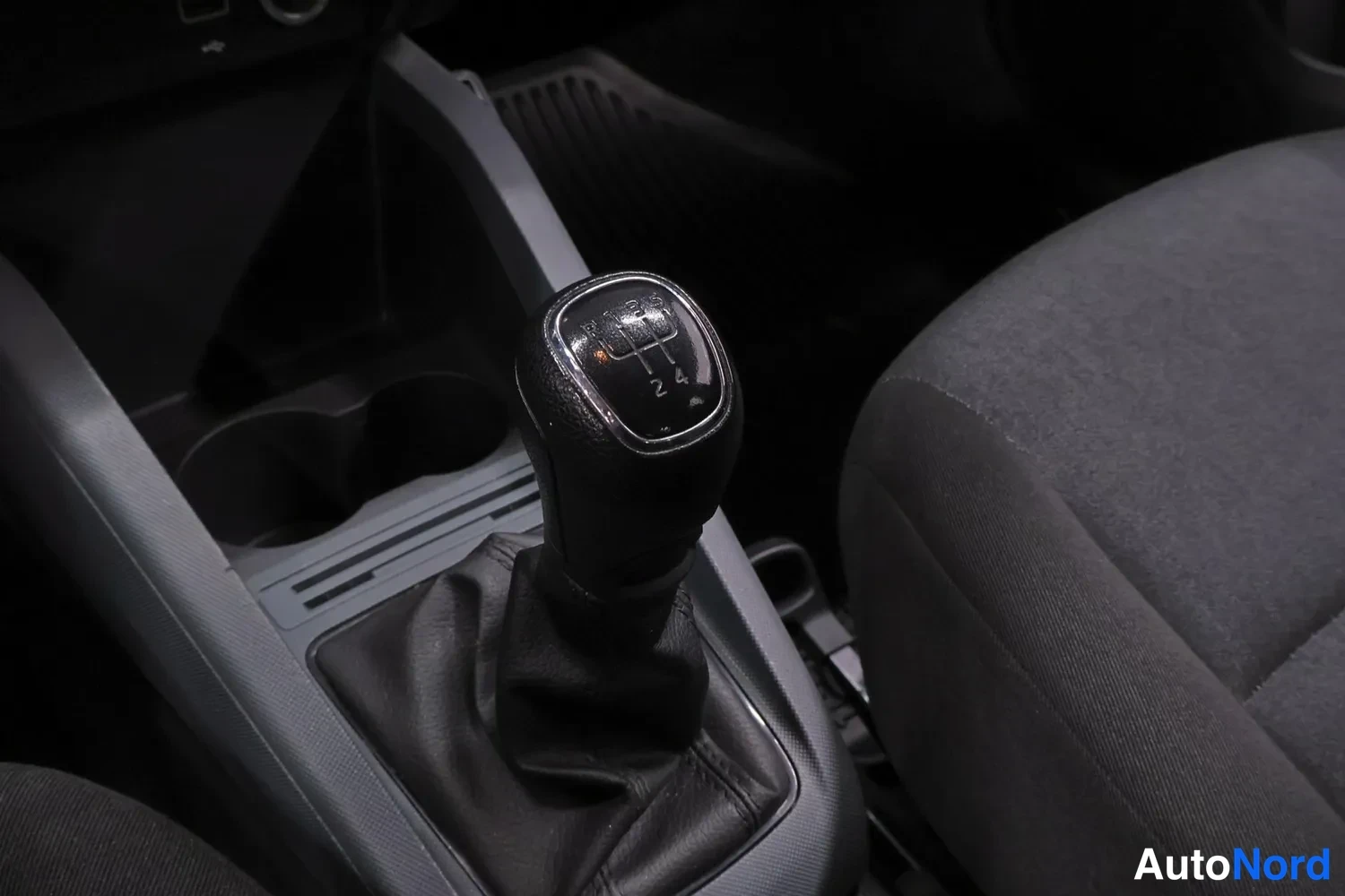 Ohjaamo: Center console area showing a 5-speed manual gear shift knob with an automatic parking brake lever to its right.