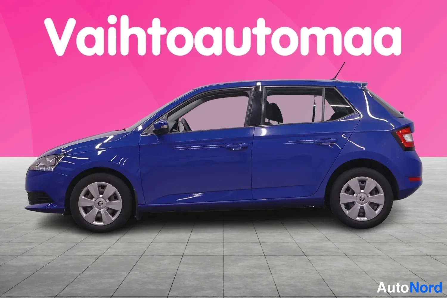Sivulta: Sininen Skoda Fabia -henkilöauto sivulta kuvattuna, viisiovinen hatchback, vaalea lattia ja pinkki tausta.