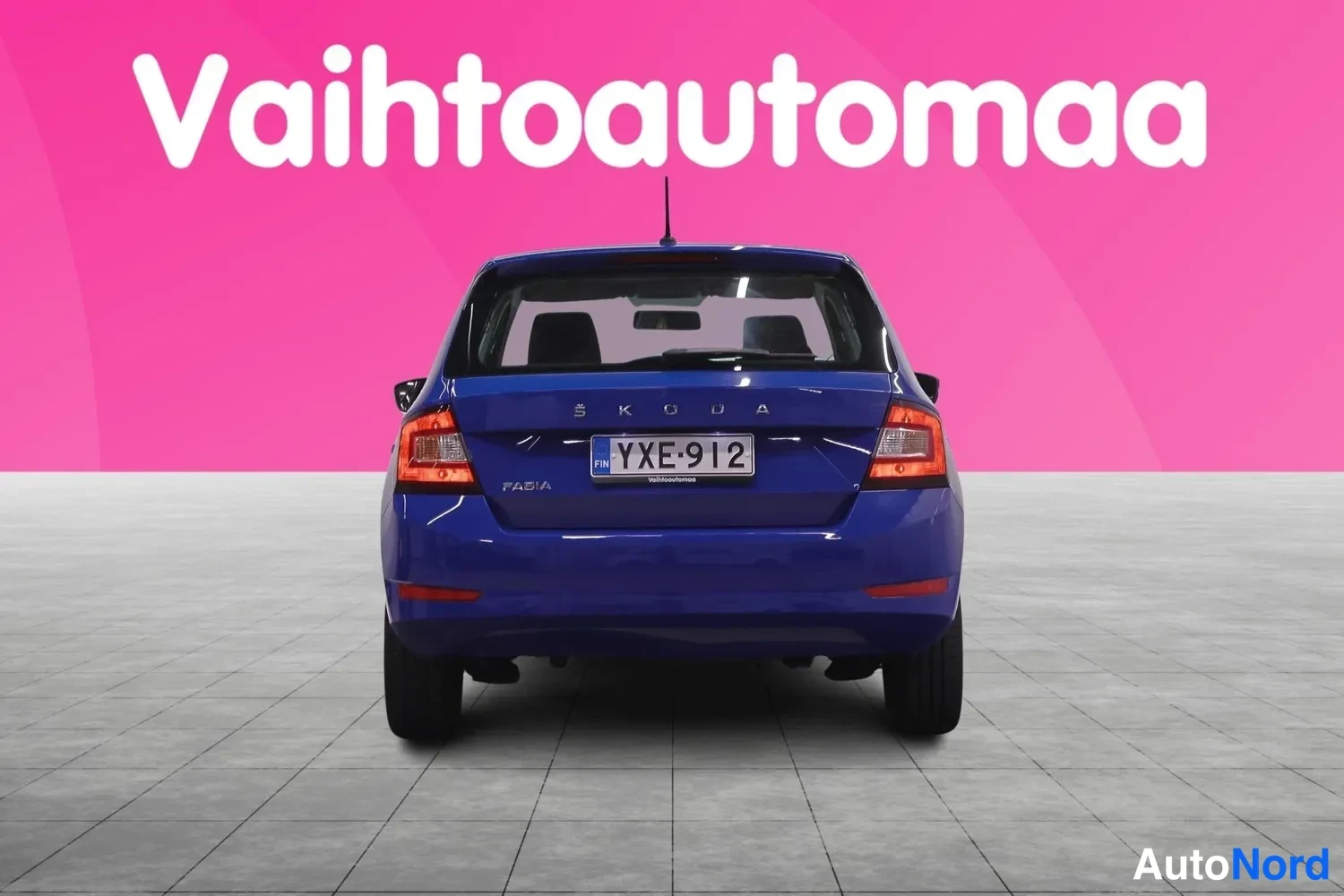 Takaa: Sininen Skoda Fabia -henkilöauto suoraan takaa kuvattuna, ŠKODA-merkintä, FABIA-tunnus ja rekisteritunnus, pinkki tausta.