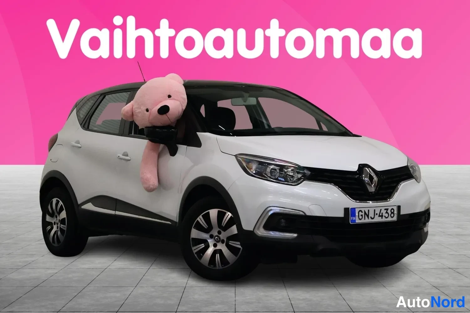 Etuviisto, nokka oikealle: Valkoinen Renault Captur kolmannelta kulmalta edestä, keulakko oikealla, rekisterillä, vaaleanpunaisella taustalla.