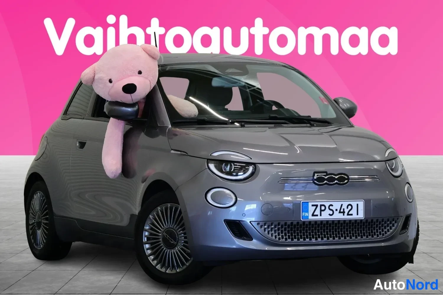 Etuviisto, nokka oikealle: Harmaan Fiat 500:n nokka oikealla ja kylki vasemmalla, rekisteritunnus, suurvaaleanpunainen tausta.