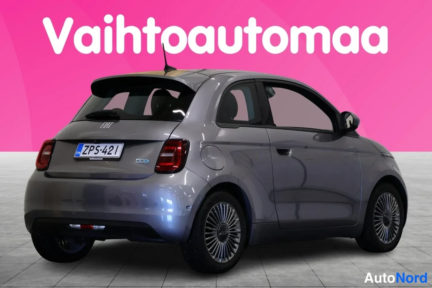 Takaviisto: Harmaa Fiat 500 kuvattuna takakulmasta vasemmalta: tavaratilan kannessa FIAT- ja 500-merkinnät, rekisterikilpi, takavalot ja vasen kylki näkyvät. Pinkki tausta