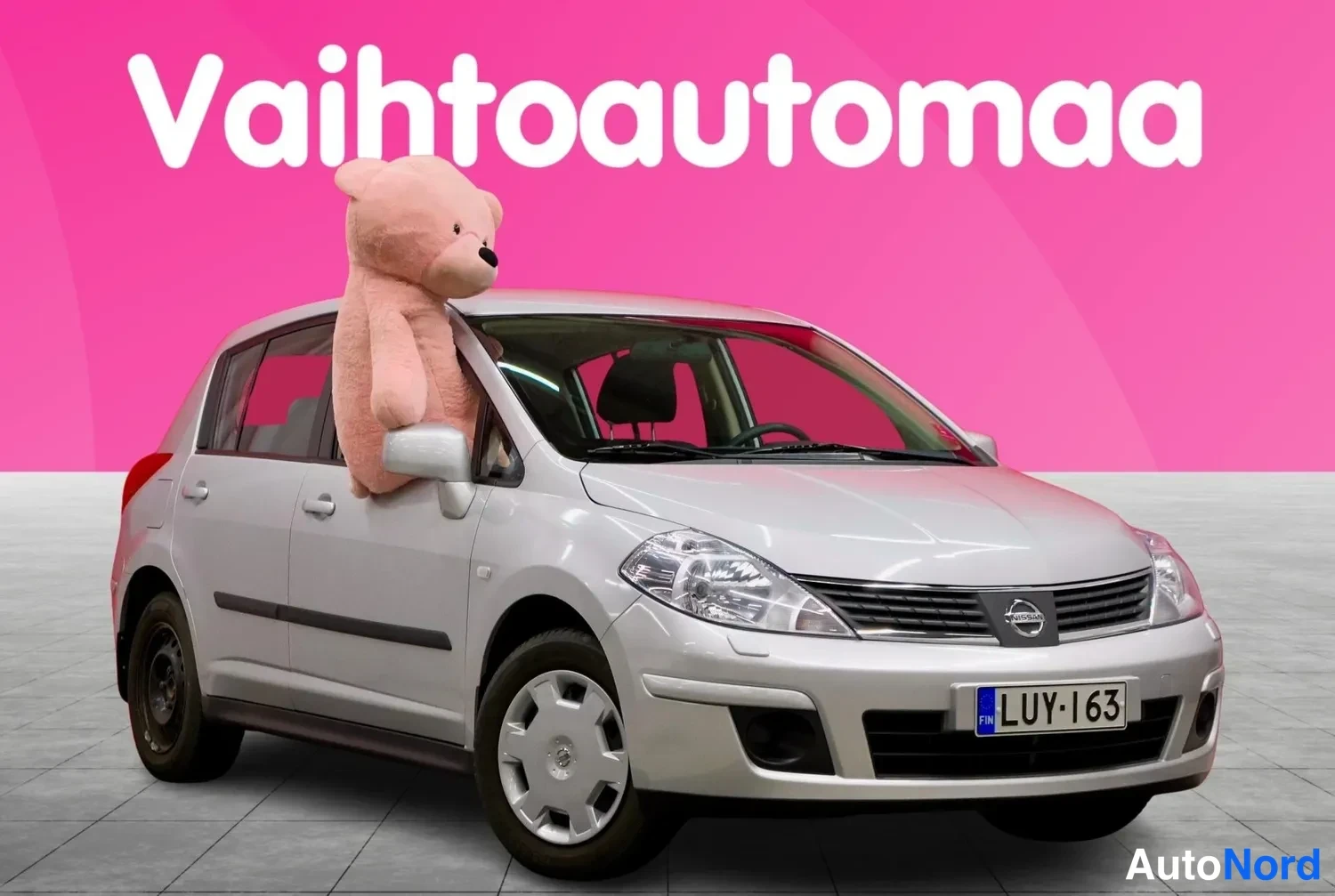 Etuviisto, nokka oikealle: Hopeinen Nissan Tiida -henkilöauto etukulmasta, rekisterikilpi