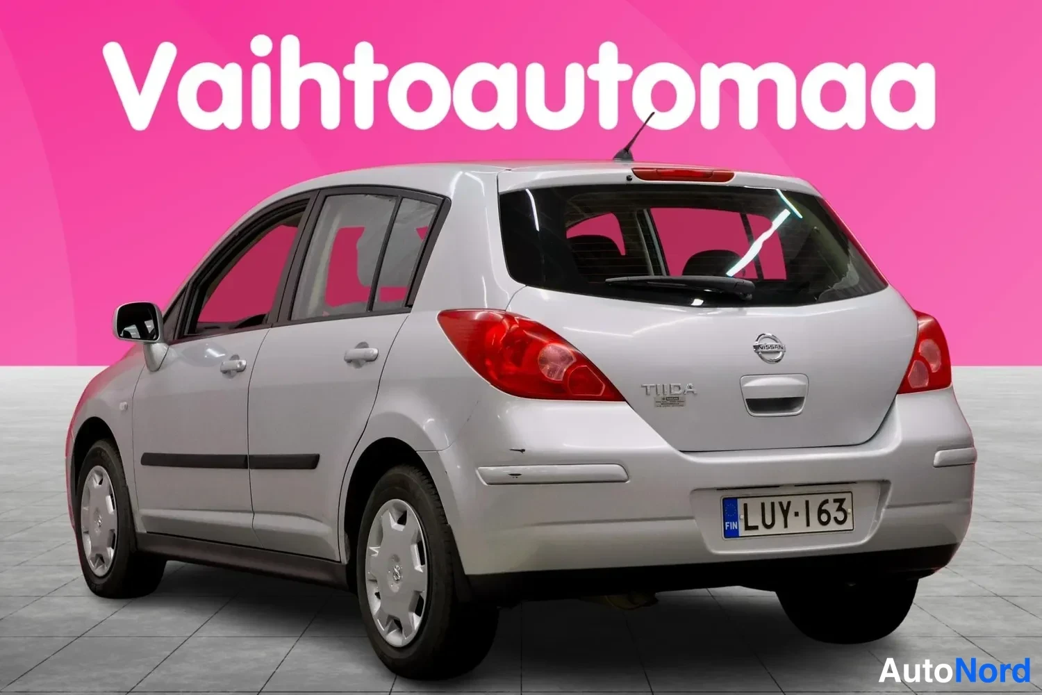 Takaviisto: Hopeanvärinen Nissan Tiida -viistoperä takaa vasemmalta kuvattuna, rekisterikilpi.