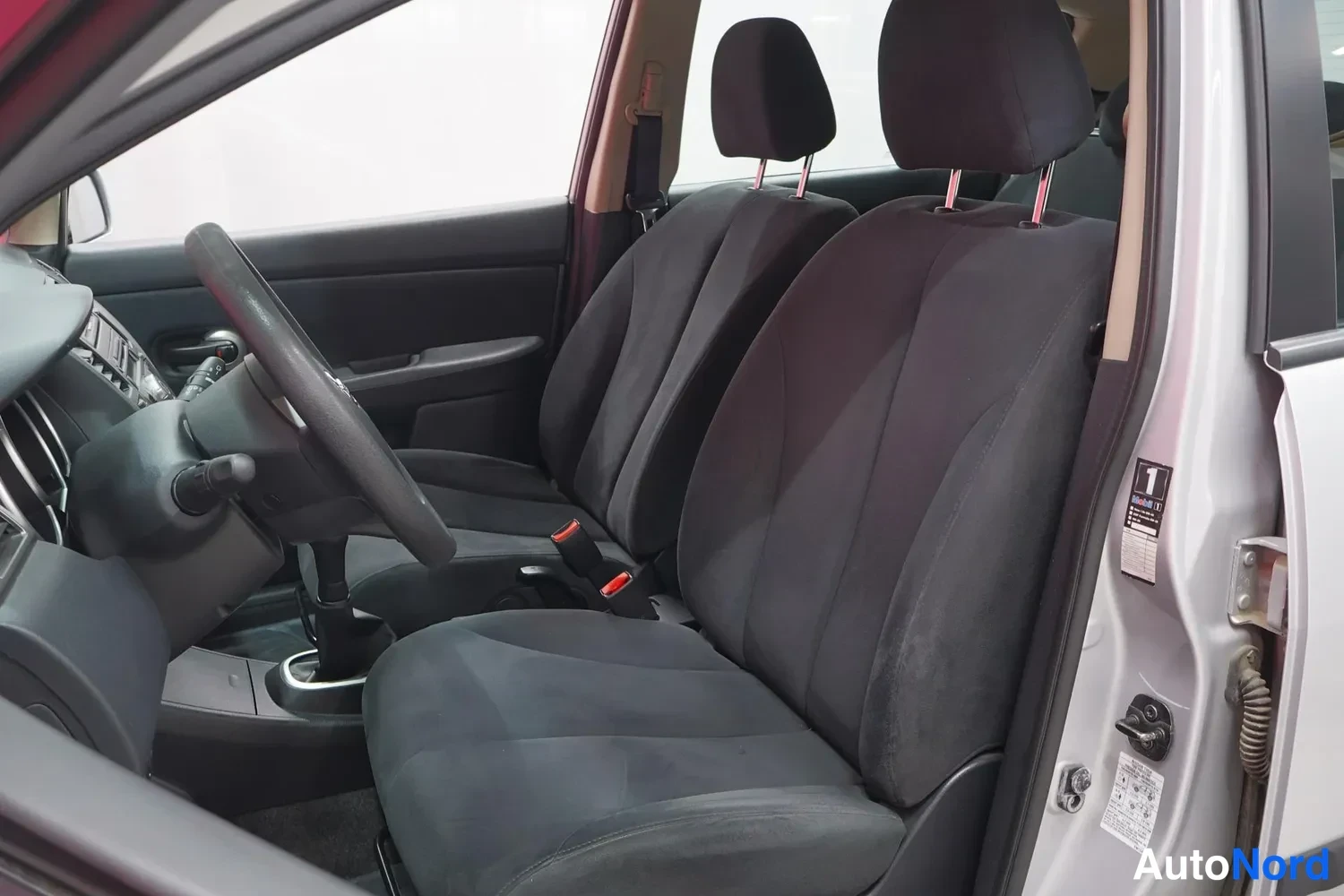 Muu: Nissan Tiidan etusisällä: tummat kankaistuolit, ohjauspyörä ja käsijarru.