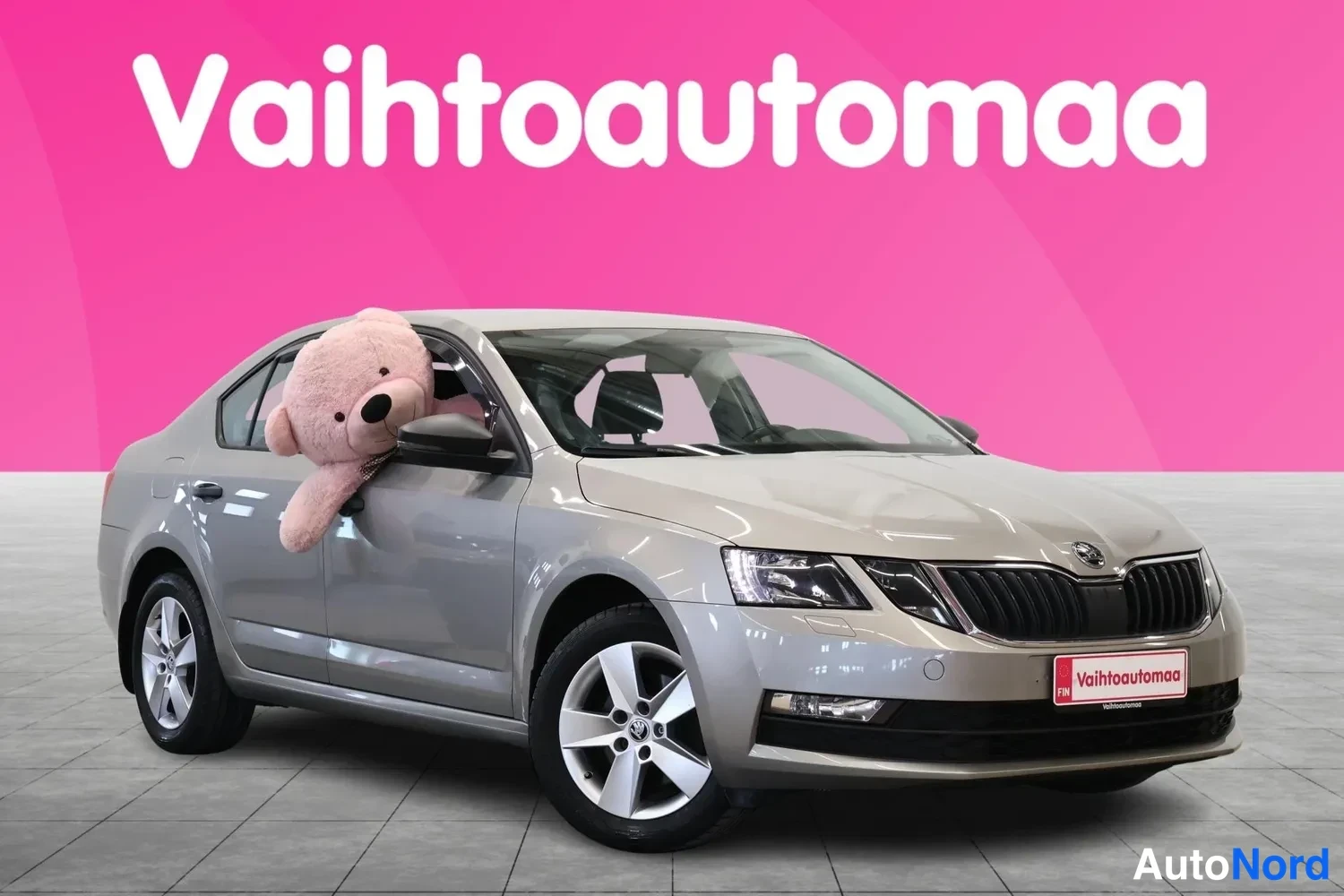 Etuviisto, nokka oikealle: Vaaleanbeige Skoda Octavia -sedan etukulmasta oikealta, keulakoodi ja oikea kylki näkyvissä; pinkki tausta ja markkinointiteksti.
